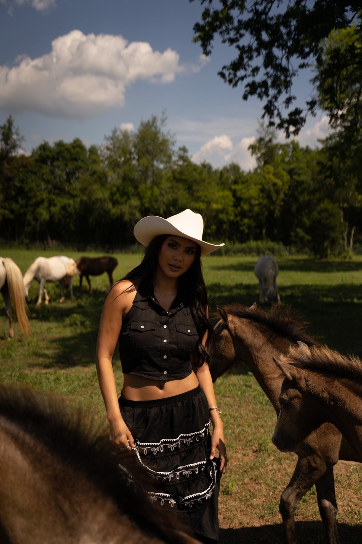 Woman in a white cowboy hat with horses wearing the H Bar C Coachella black embroidered skirt and a black top.