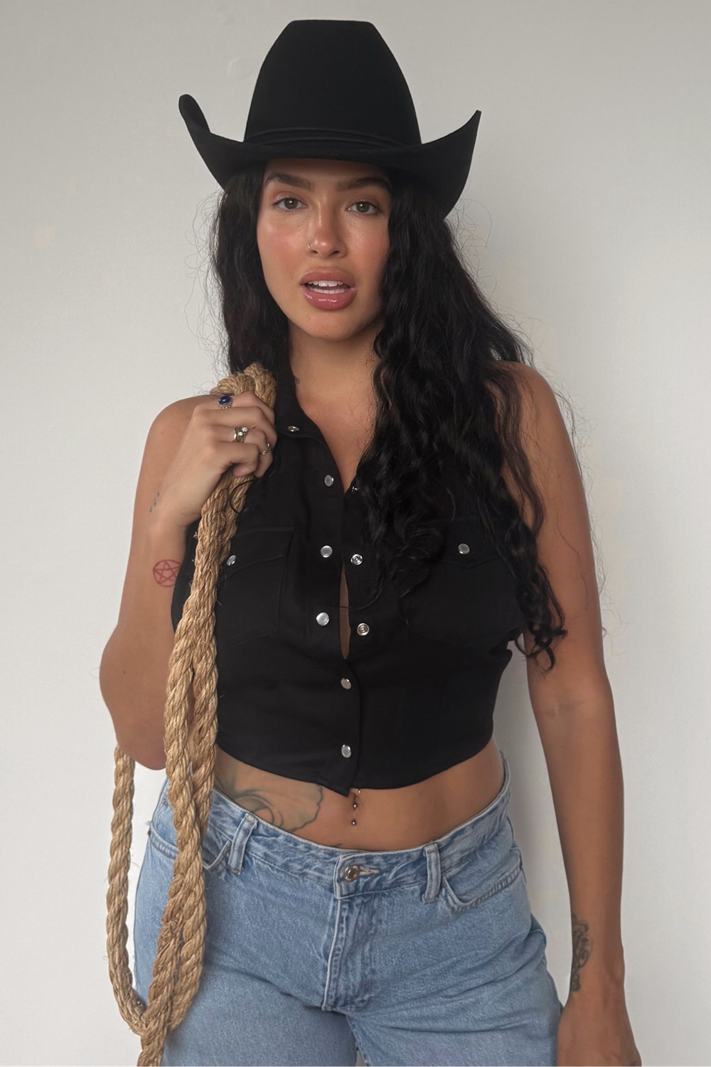 Woman holding a lasso wearing the H Bar C Hampton black halter top, a 1970s inspired western backless top, with jeans.