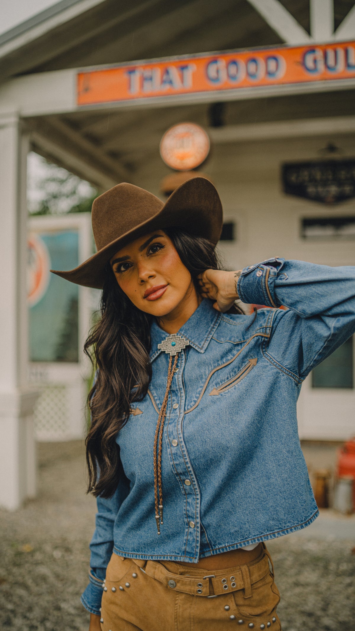Woman in a brown cowboy hat wearing the Rustler x H Bar C women's denim cropped western shirt.