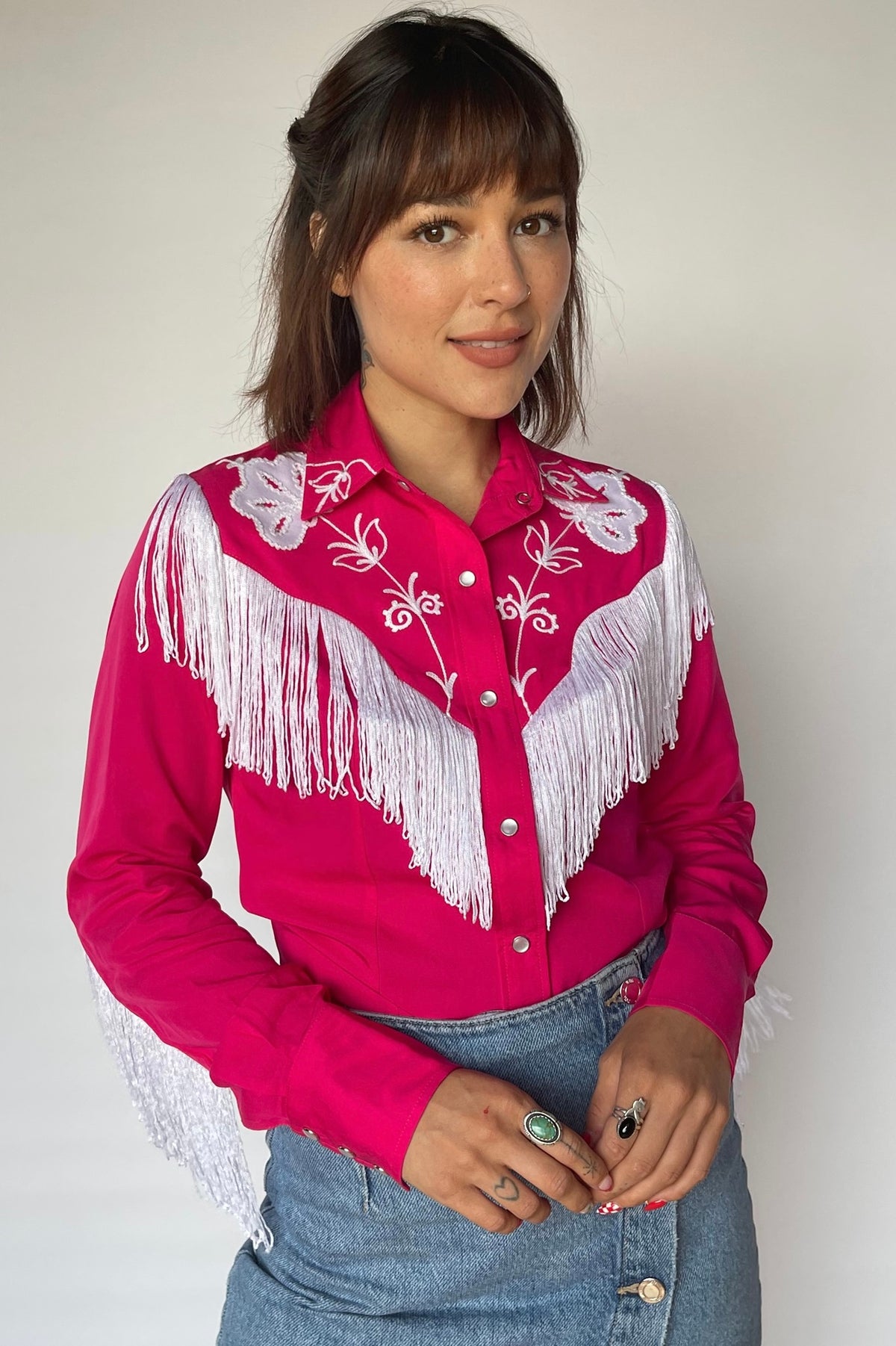 Woman wearing the H Bar C Taos women's shirt in pink with white fringe and embroidery on the yoke and sleeves, from the Hollywood Collection.