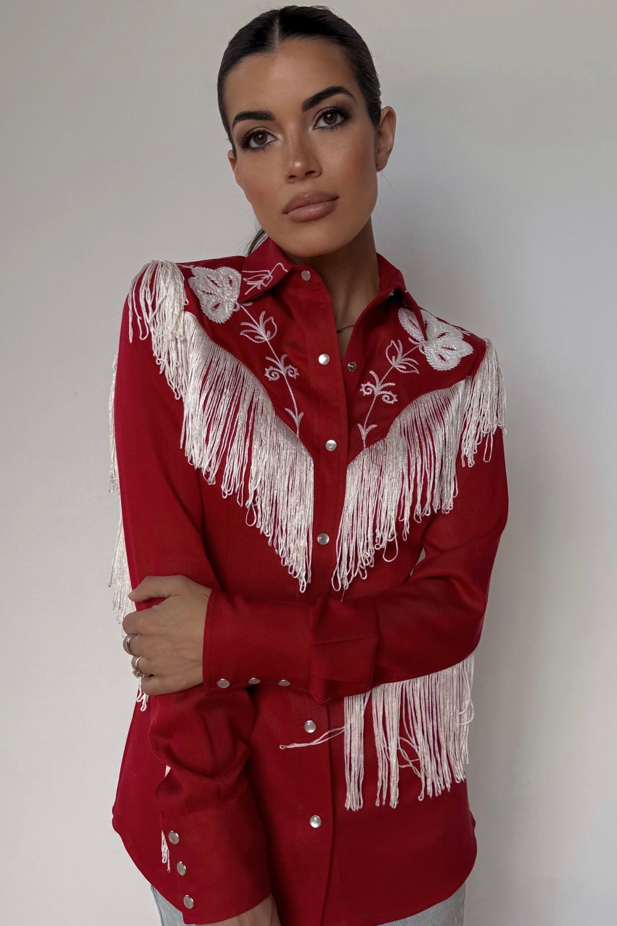 Woman wearing the H Bar C Taos women's shirt in red with white fringe and embroidery on the yoke and sleeves.