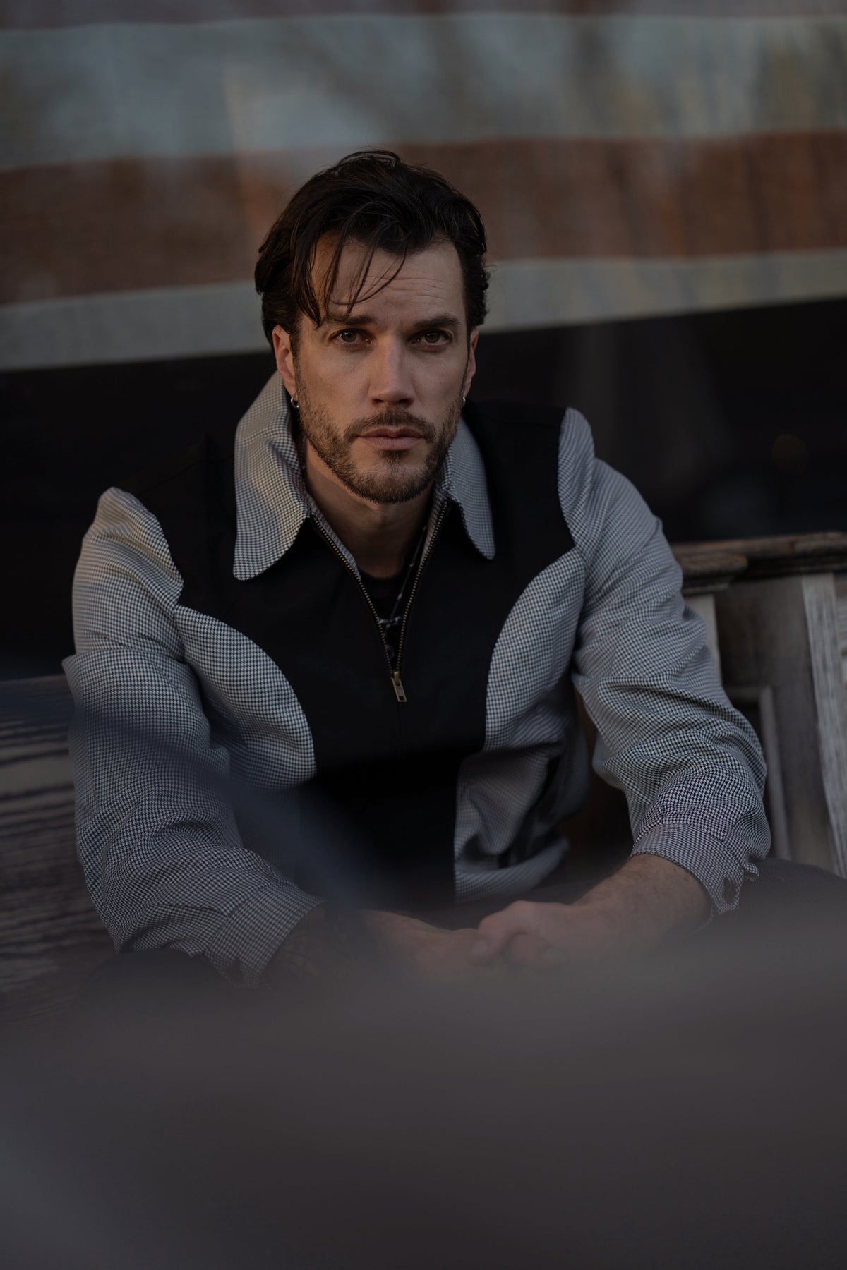 Man seated on a wooden bench wearing the H Bar C Kentucky black houndstooth jacket.