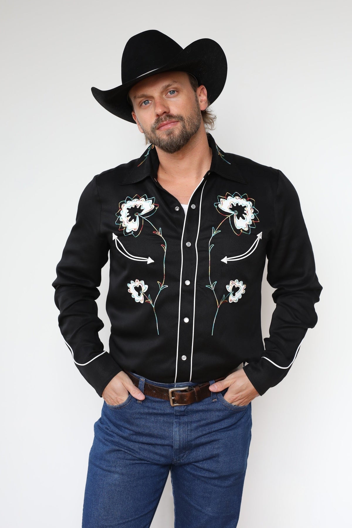 Man in a black cowboy hat wearing the H Bar C Texas men's shirt in black with white and turquoise floral embroidery, a 1940s H Bar C classic.