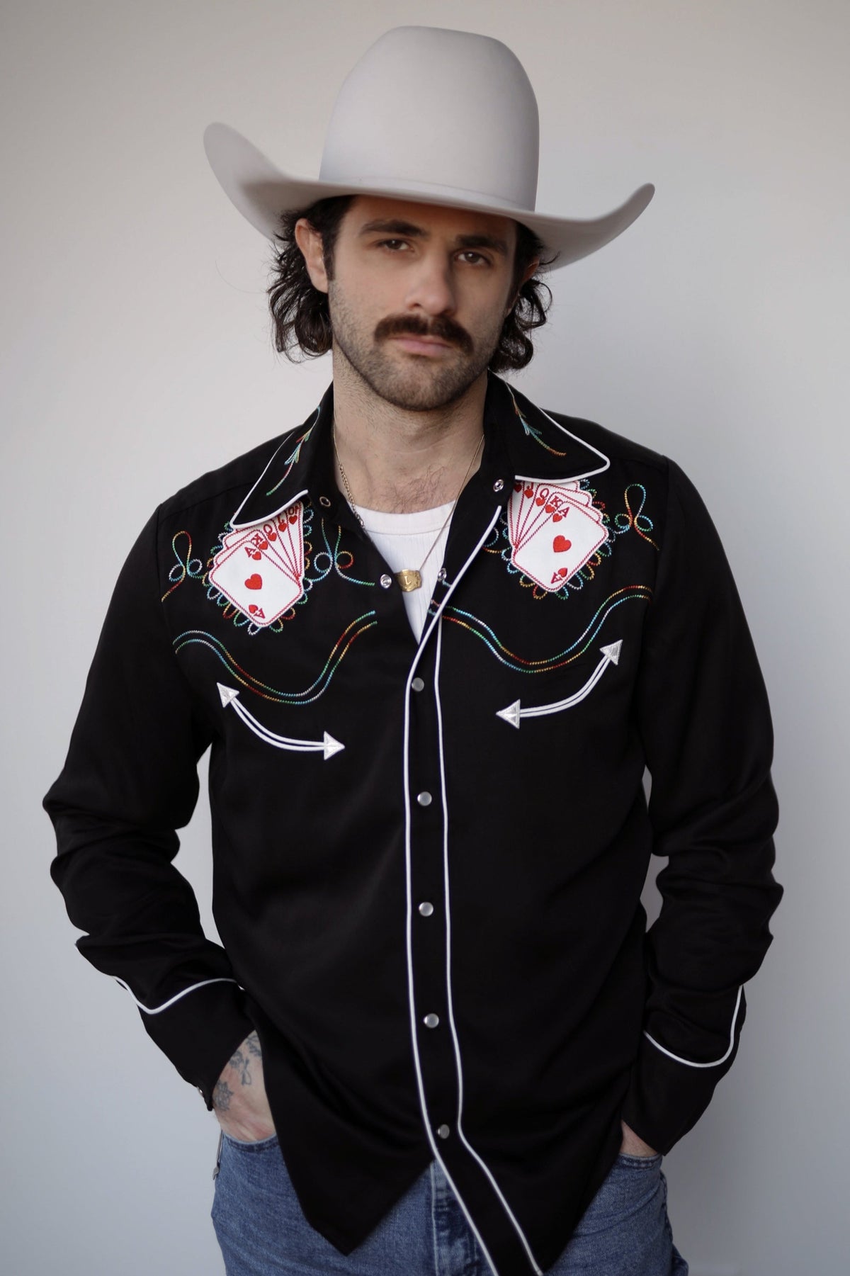 Man in a cream cowboy hat wearing the H Bar C Royal Flush shirt in black with embroidered playing cards and multicolor piping.
