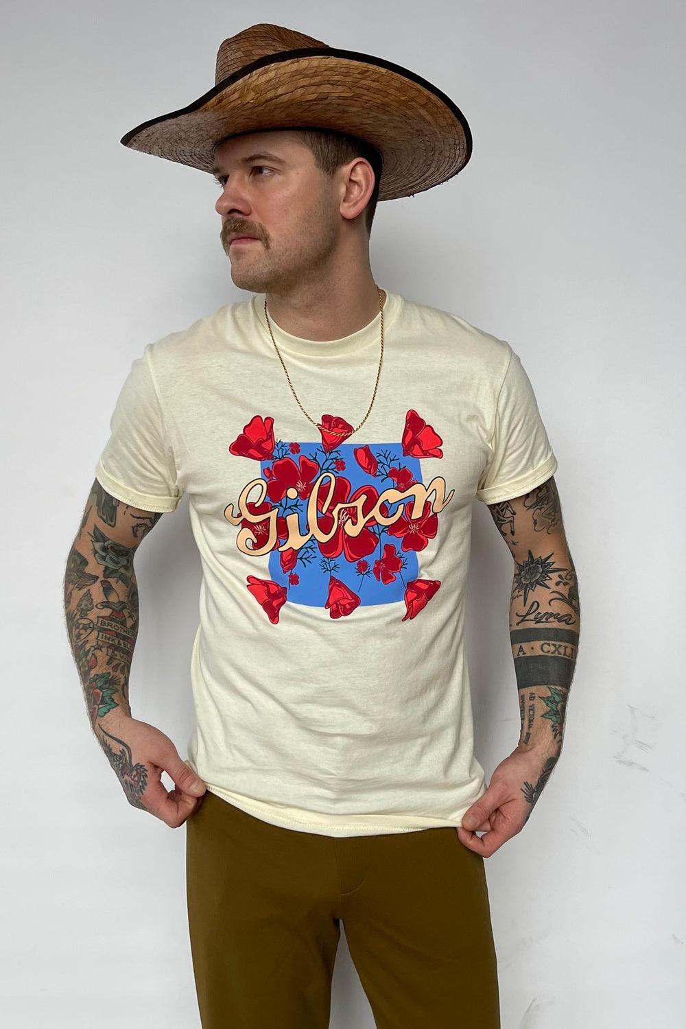 Man in a straw cowboy hat wearing the HBarC x Gibson Dove tee in cream with a red and blue Gibson dove graphic.