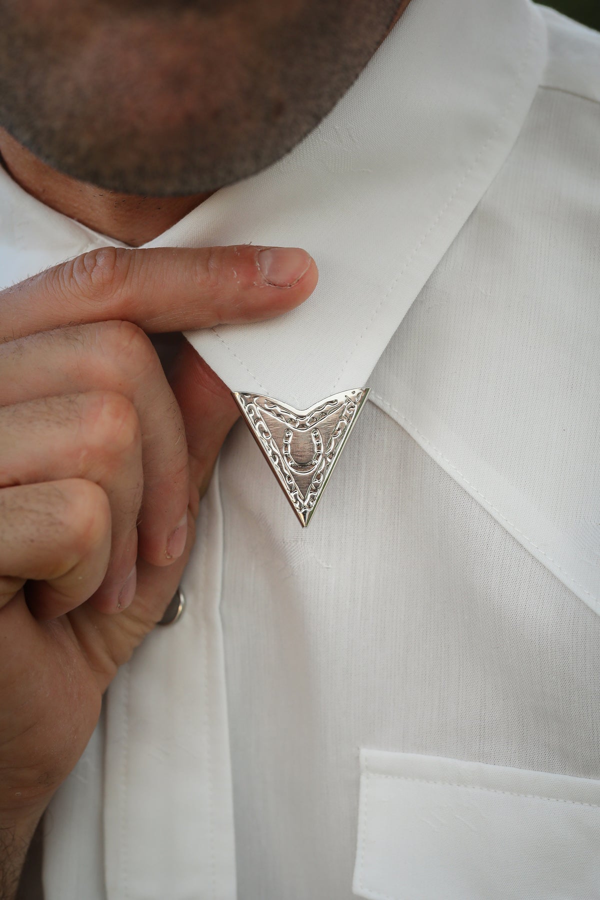 Man adjusting the H Bar C engraved silver collar tip on a white western shirt.