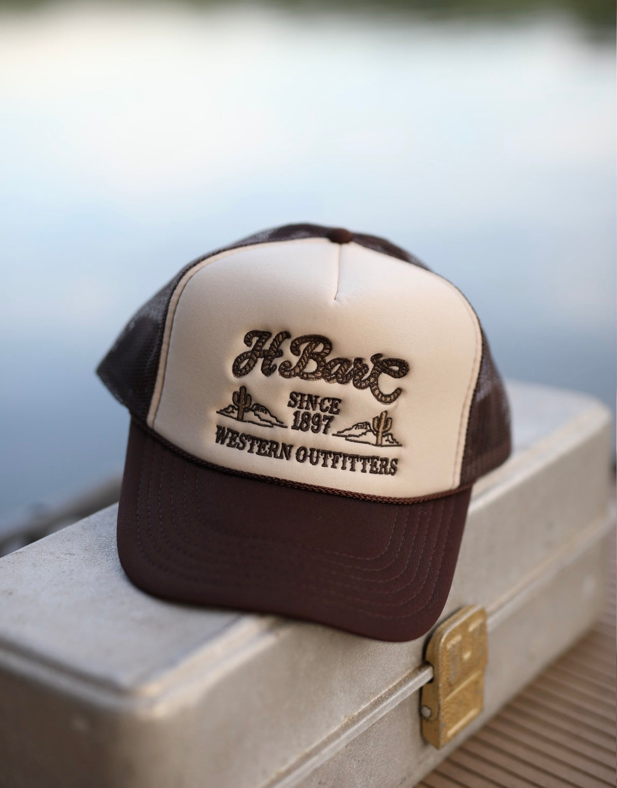 H Bar C Western Outfitters tan rope trucker hat resting on a vintage tackle box.