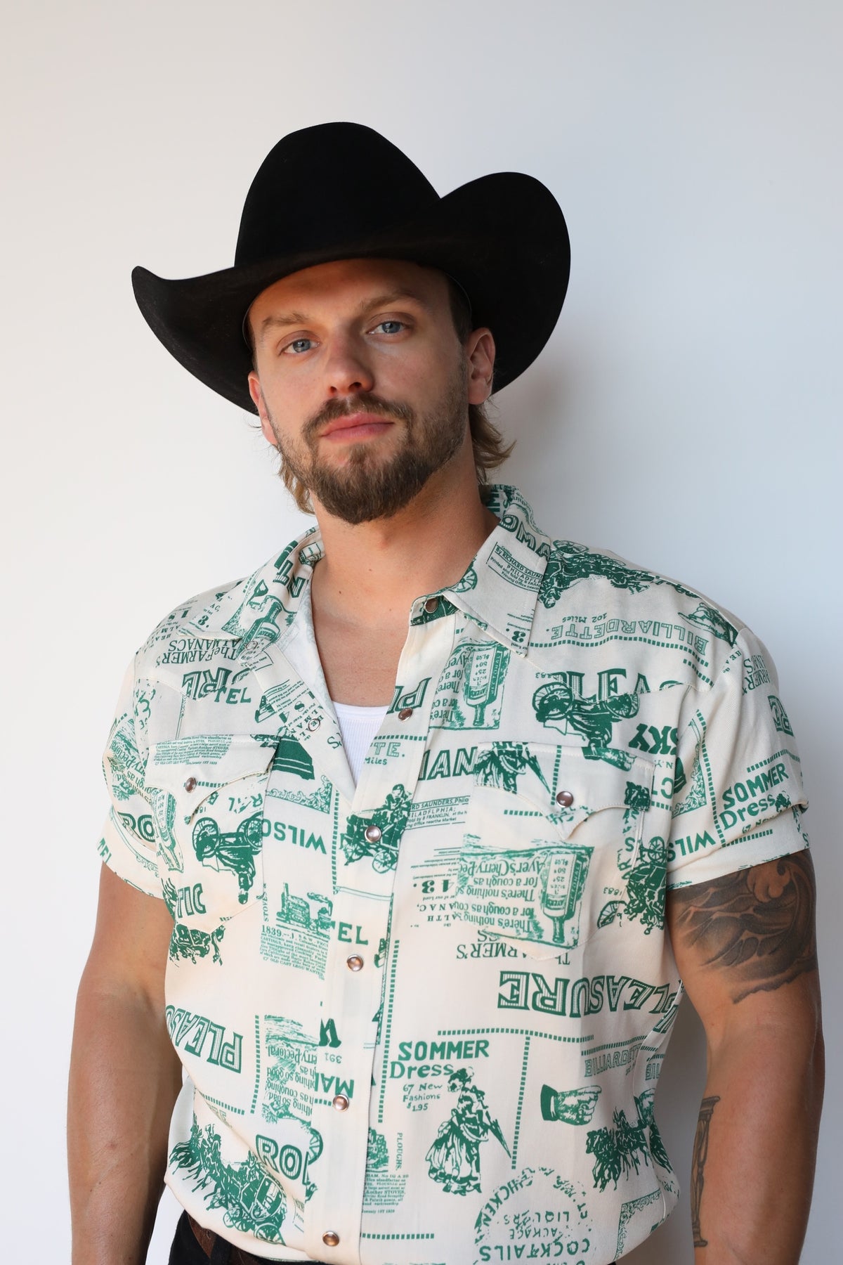 Front view of the H Bar C Newport Somerville cream and green print snap shirt with a black hat.