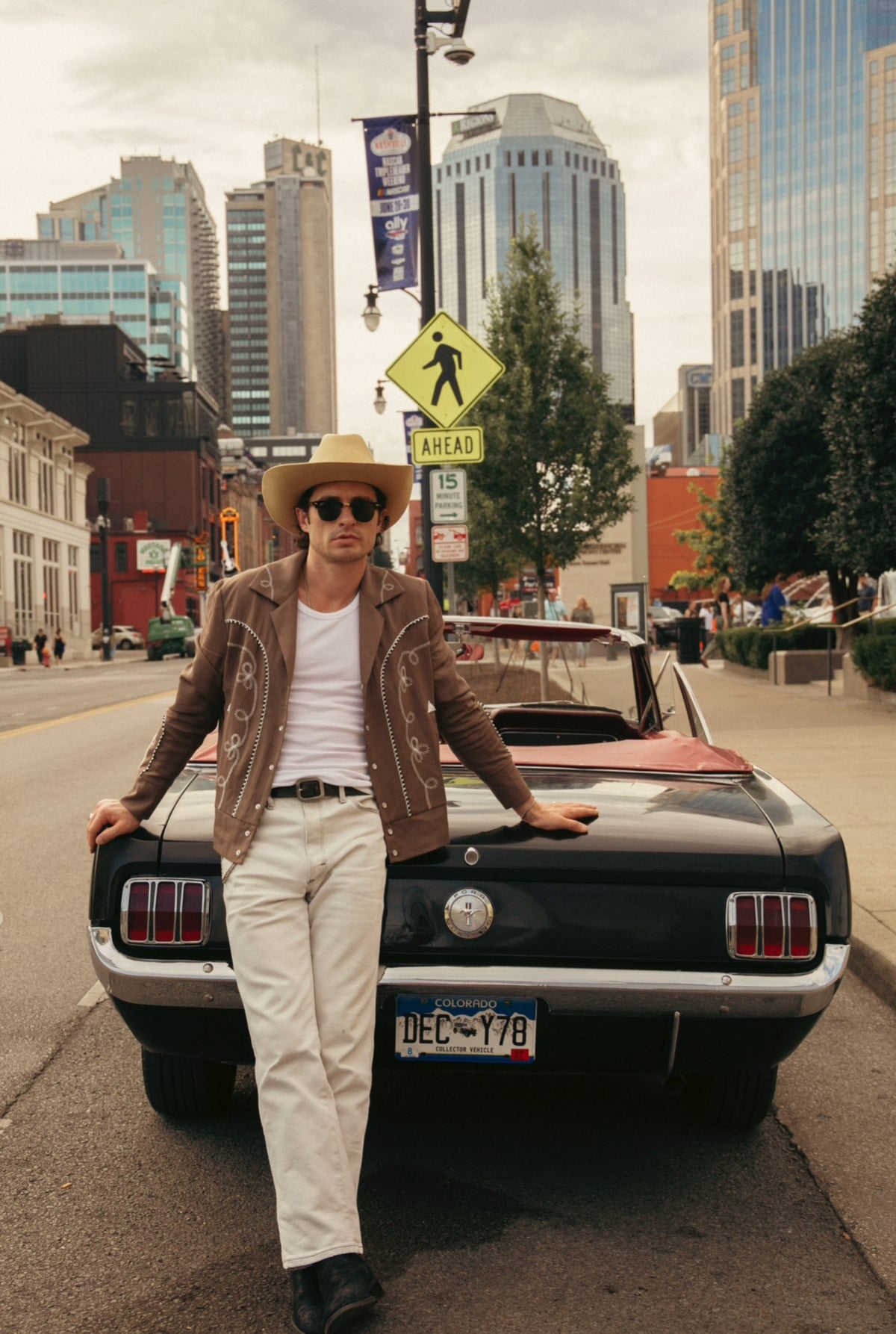 Man wearing the H Bar C Bolero cocoa and white jacket and cream pants, leaning on a vintage black Mustang in downtown Nashville.
