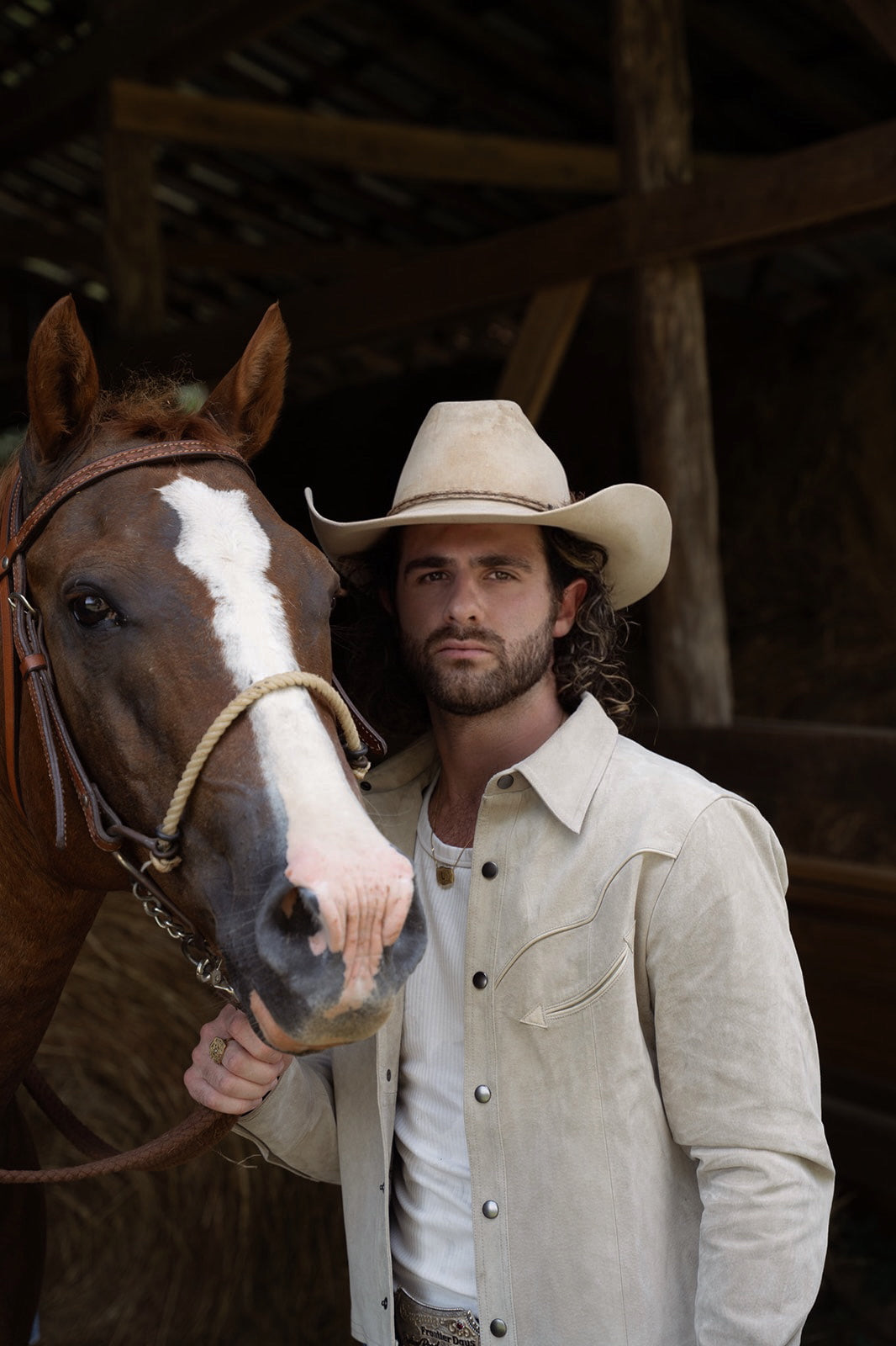 Man in a cowboy hat beside a horse in a barn wearing the H Bar C Austin stone suede western jacket.