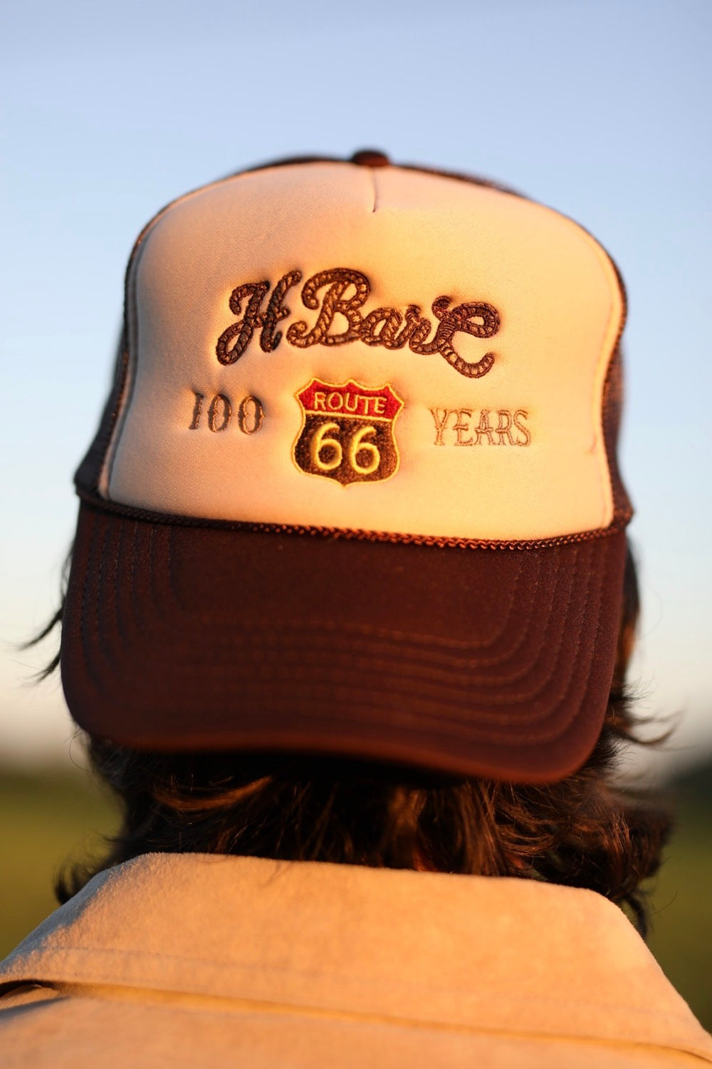 H Bar C trucker baseball hat in tan and brown with a 100 Years Route 66 shield logo.