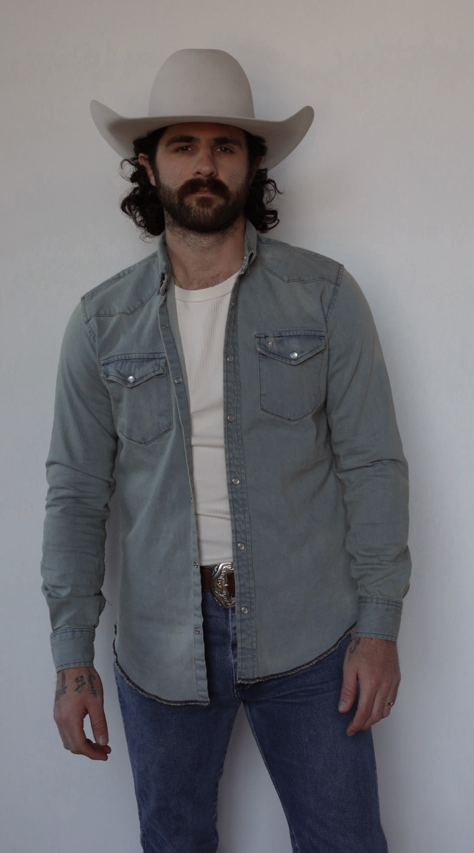 Man wearing the H Bar C Resurgent western shirt open over a white tee with jeans and a cream hat.