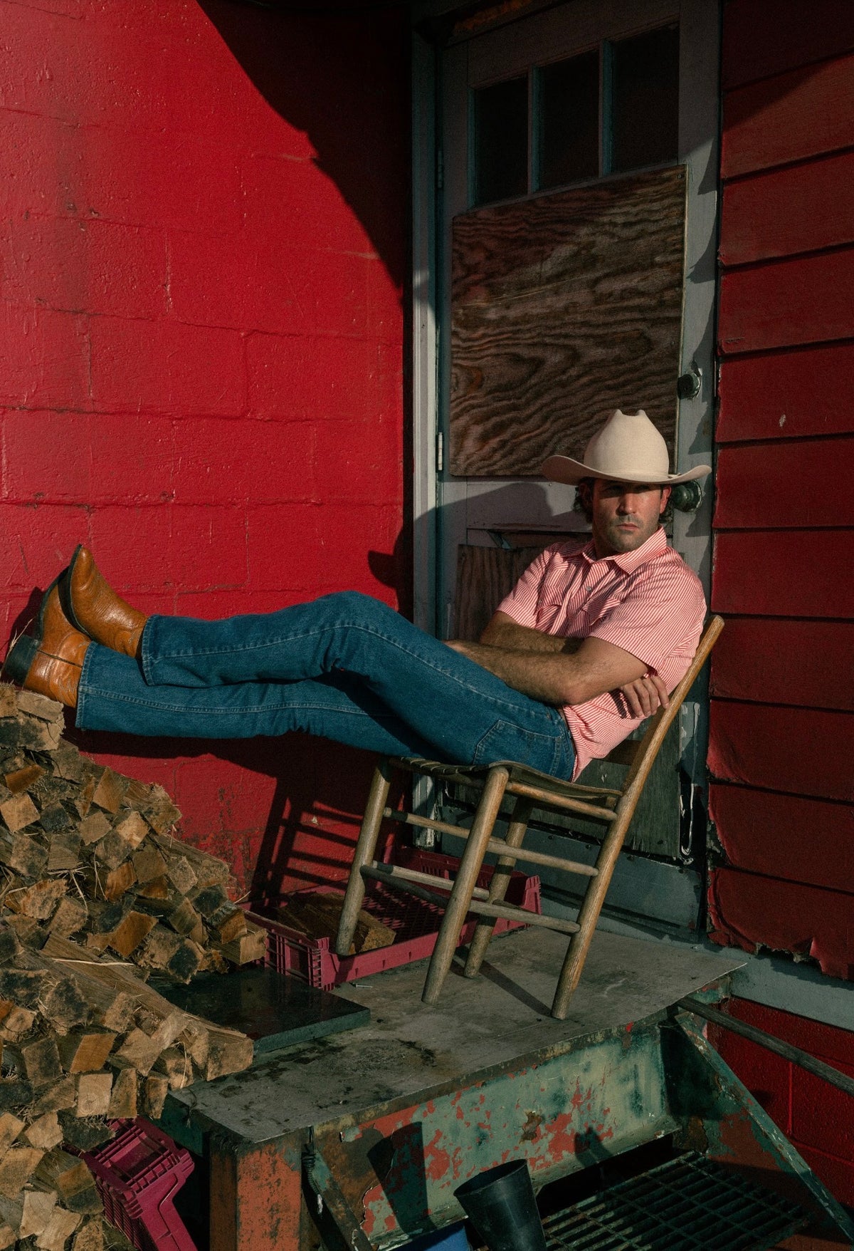 Man relaxing in a chair by a red barn wearing the H Bar C Newport red striped shirt and jeans.