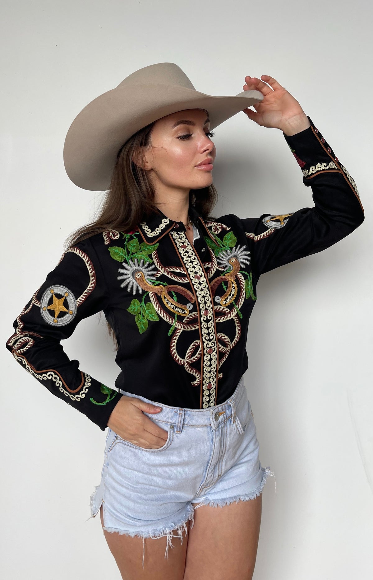 Woman wearing the H Bar C Catalina black embroidered western shirt with denim shorts and a cowboy hat.