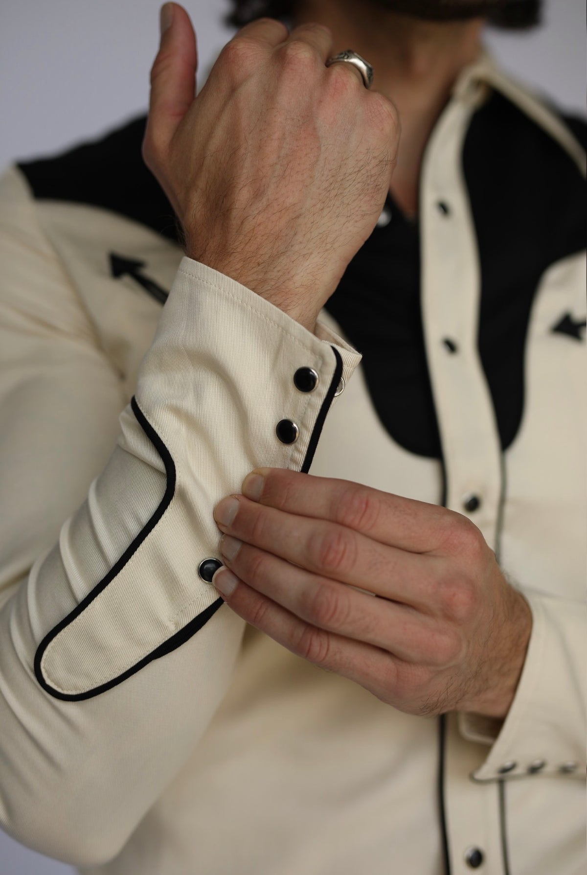 Cuff detail of the H Bar C San Juan off-white shirt with black piping and pearl snaps.