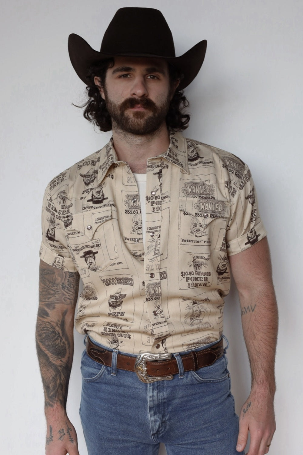 Man in a black cowboy hat wearing the H Bar C Newport Tumbleweed short sleeve western shirt in a cream and brown novelty print.