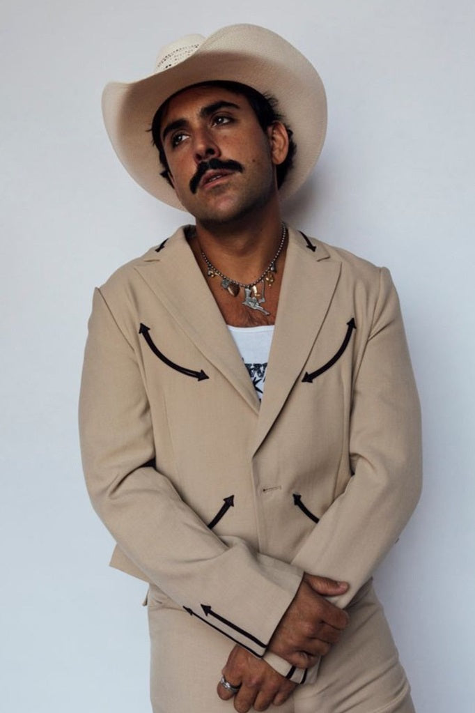 Man in a cream cowboy hat wearing the H Bar C Calamity tan western jacket with brown arrows.