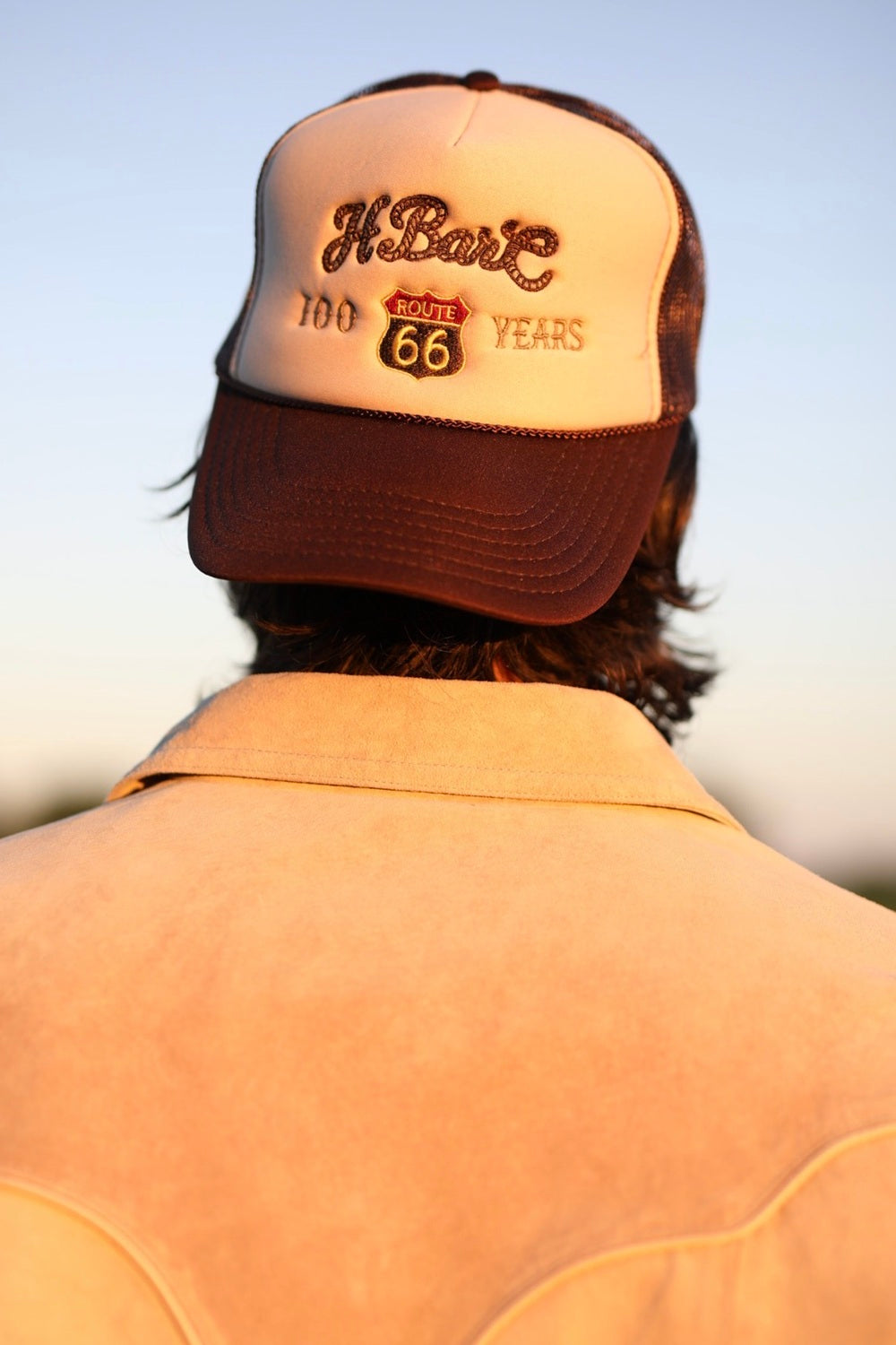Back of a man wearing the H Bar C tan 66 shield trucker hat with a brown bill.