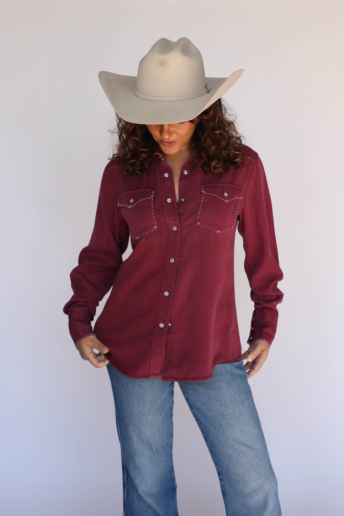 Woman in a cream cowboy hat wearing the H Bar C Brooklyn women's shirt in wine with contrast stitching and pearl snaps.