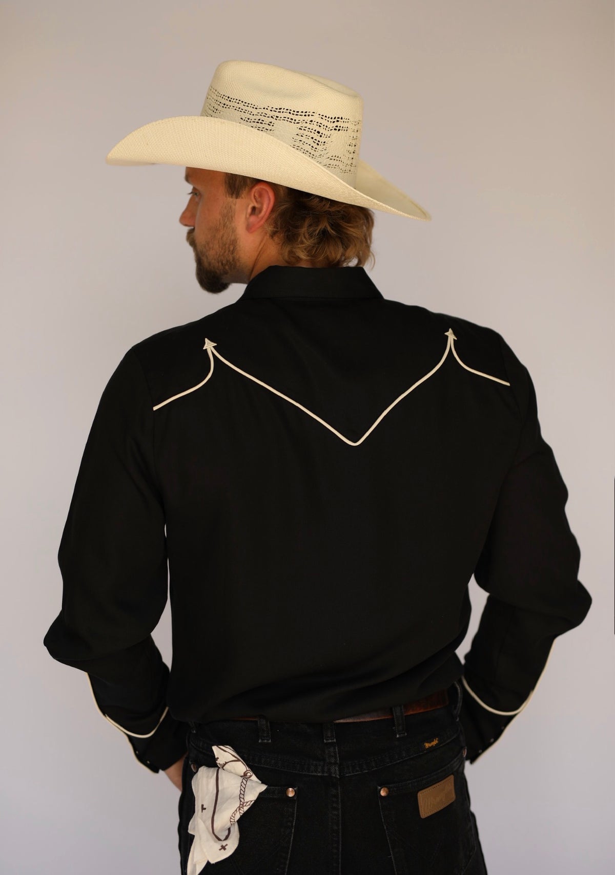 Back view of the H Bar C Reno black shirt with off-white piping and a straw cowboy hat.