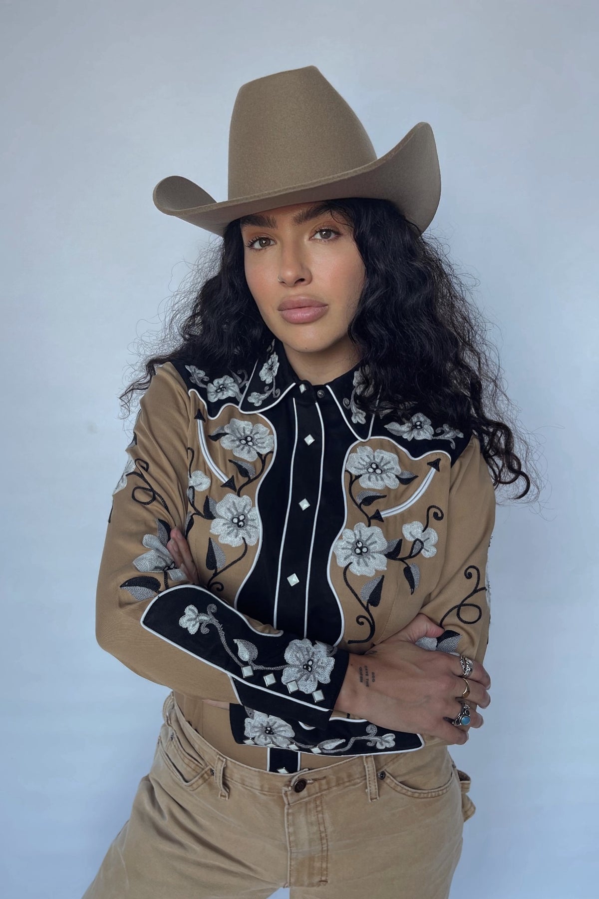 Woman in a tan cowboy hat wearing the H Bar C Santa Ana women's shirt in tan with black yokes and white floral embroidery.