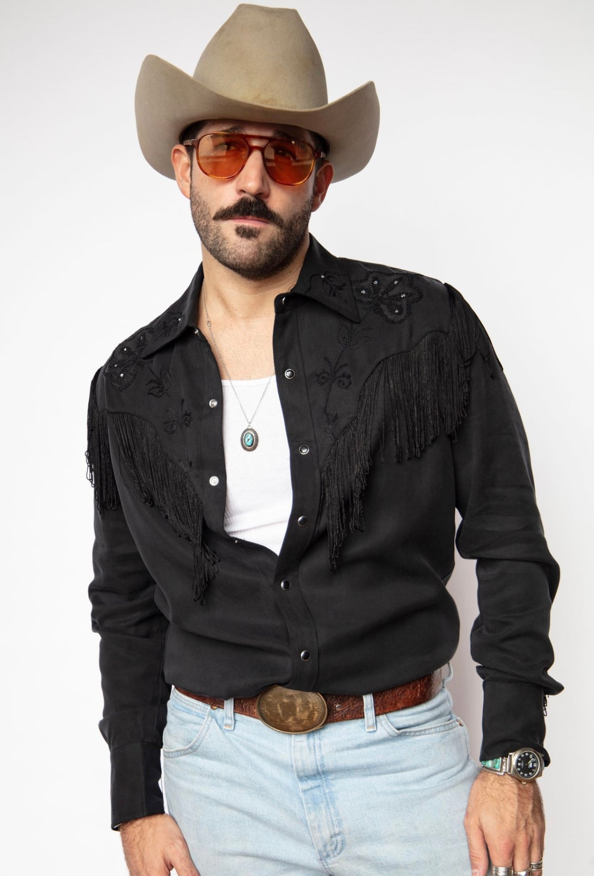 Man in a straw cowboy hat and tinted glasses wearing the H Bar C Taos all black fringe shirt with light jeans.