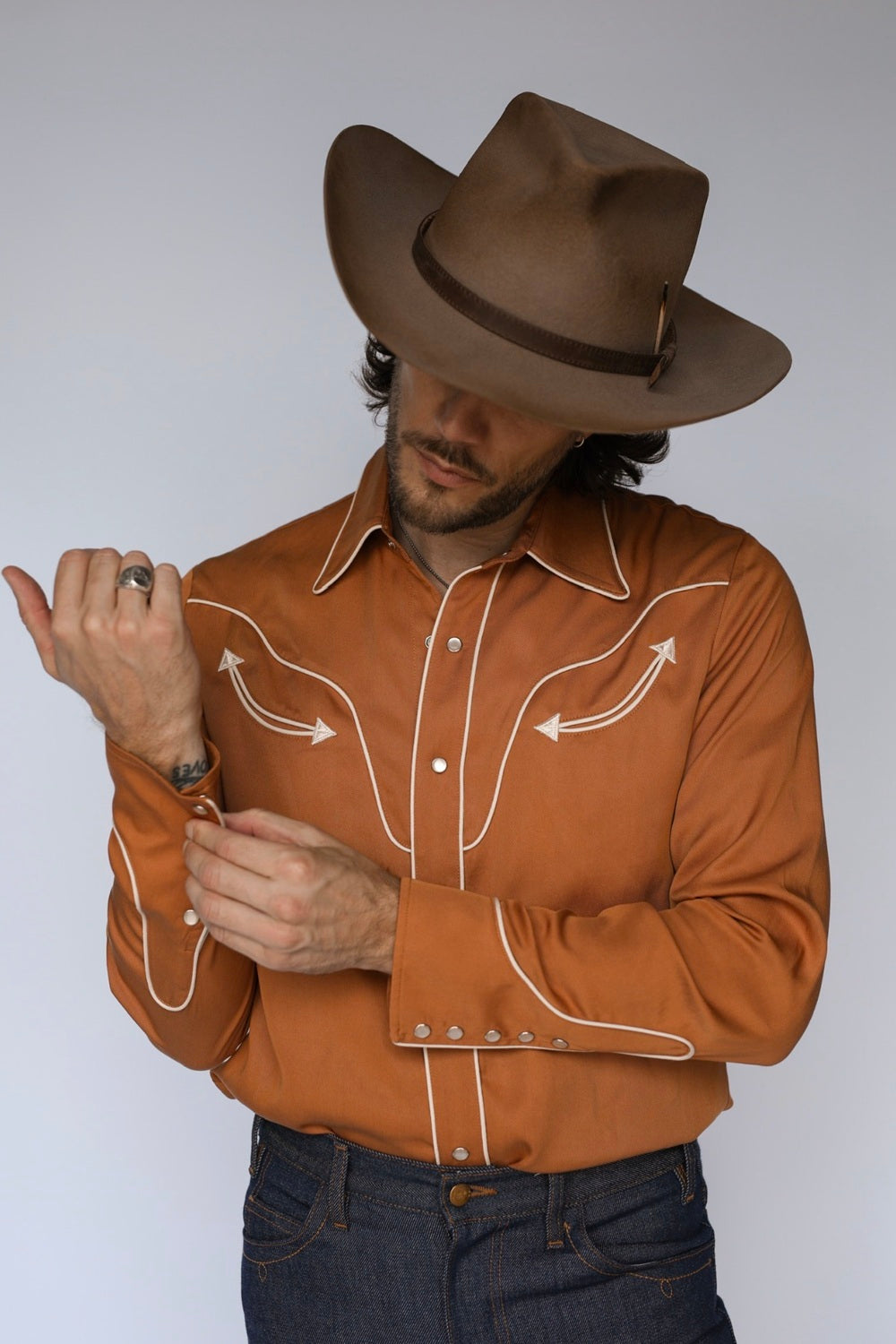 Man fastening the cuff of the H Bar C San Fernando burnt orange western shirt with cream piped yoke and rodeo cuffs.