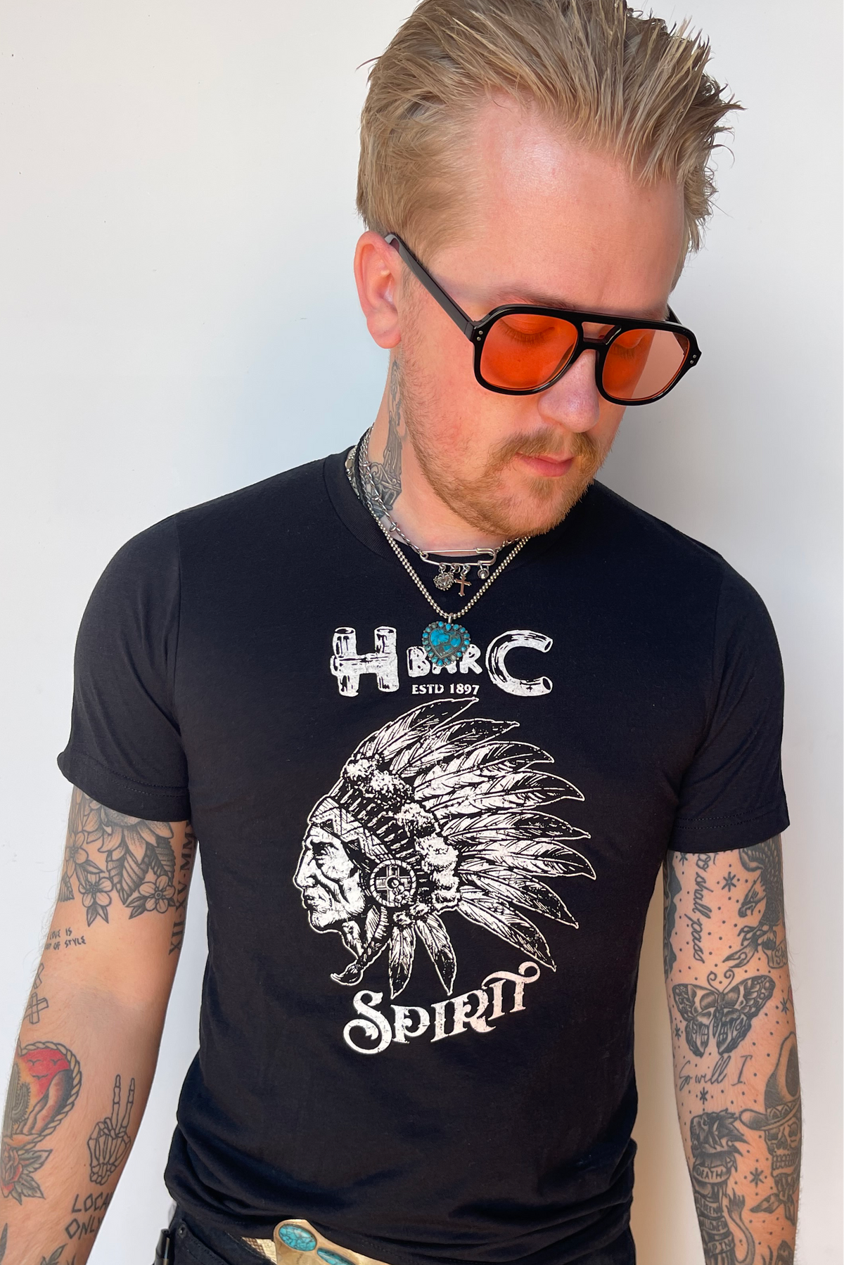Man in tinted glasses wearing the H Bar C Black Spirit T-shirt with a vintage chief graphic and turquoise H C logo.
