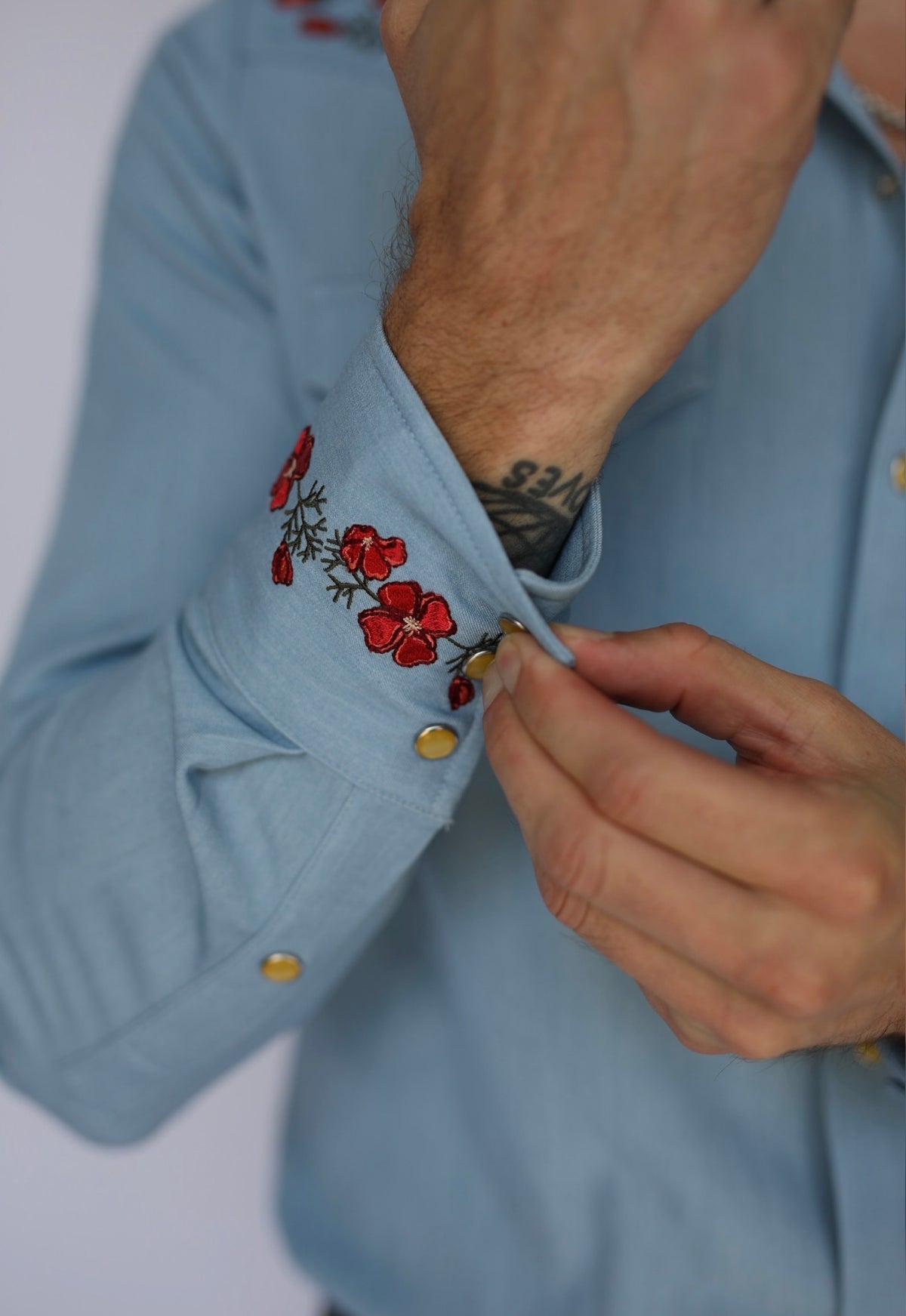 Close-up of the red poppy embroidered cuff and pearl snaps on the HBarC x Gibson Dove western shirt.
