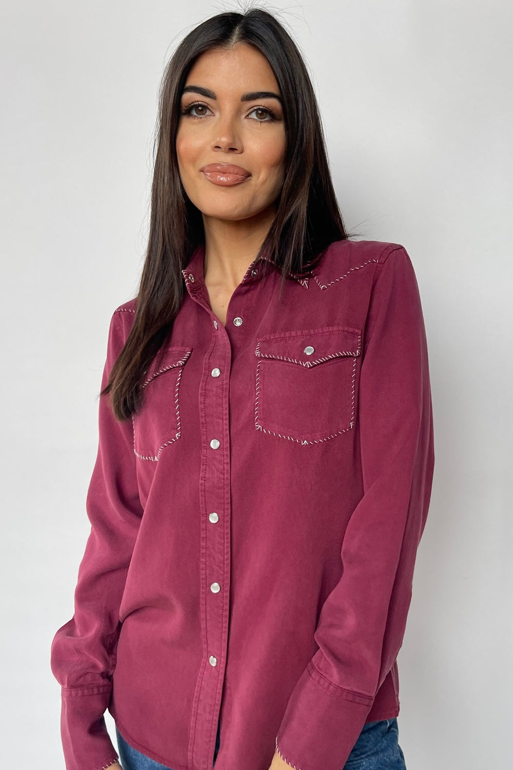 Woman wearing the H Bar C Brooklyn women's shirt in wine with accent stitched pockets and collar, with jeans.