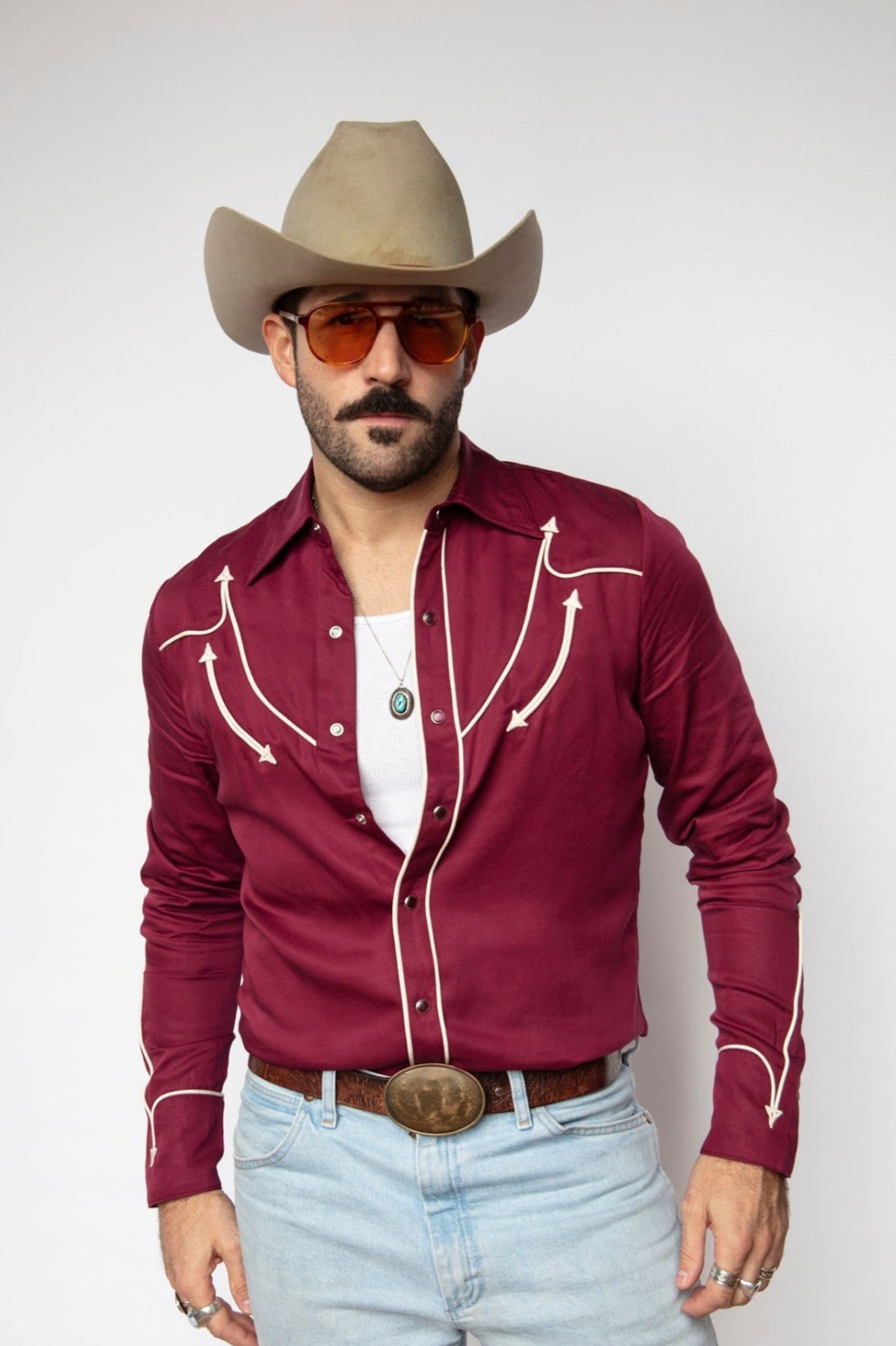 Man in a cowboy hat wearing the H Bar C Reno shirt in maroon with off white piping and arrow embroidery, with light jeans.
