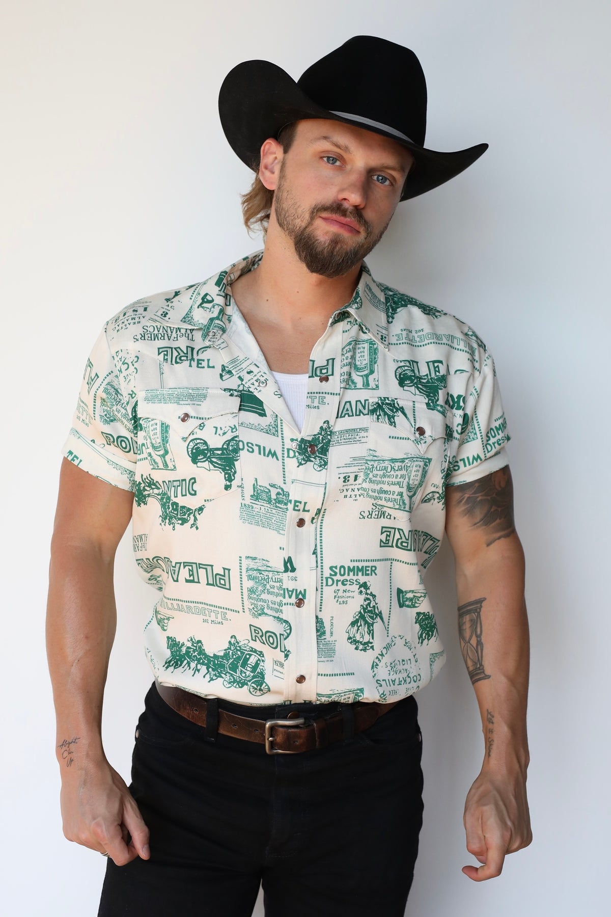 Man in a black cowboy hat wearing the H Bar C Newport Somerville short sleeve shirt in cream with a green vintage western print.