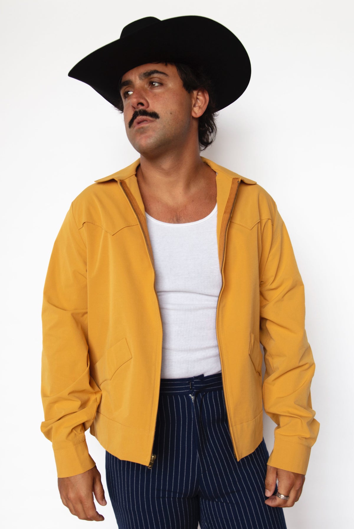 Front view of the H Bar C Mustang mustard yellow jacket worn open over a white tank with pinstripe pants.