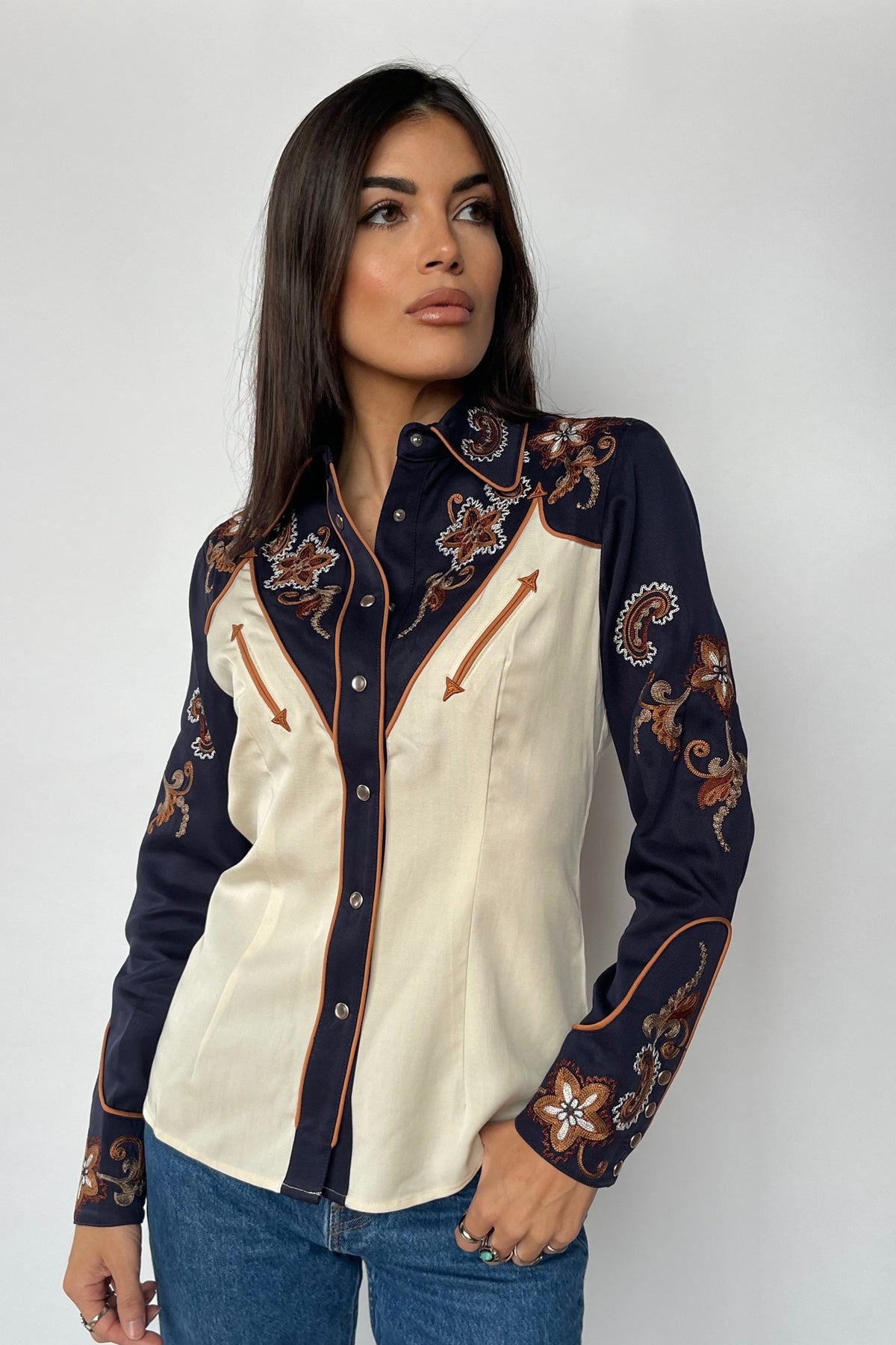 Front view of the H Bar C Aspen women's off white western shirt with navy color block and embroidered sleeves, worn with jeans.