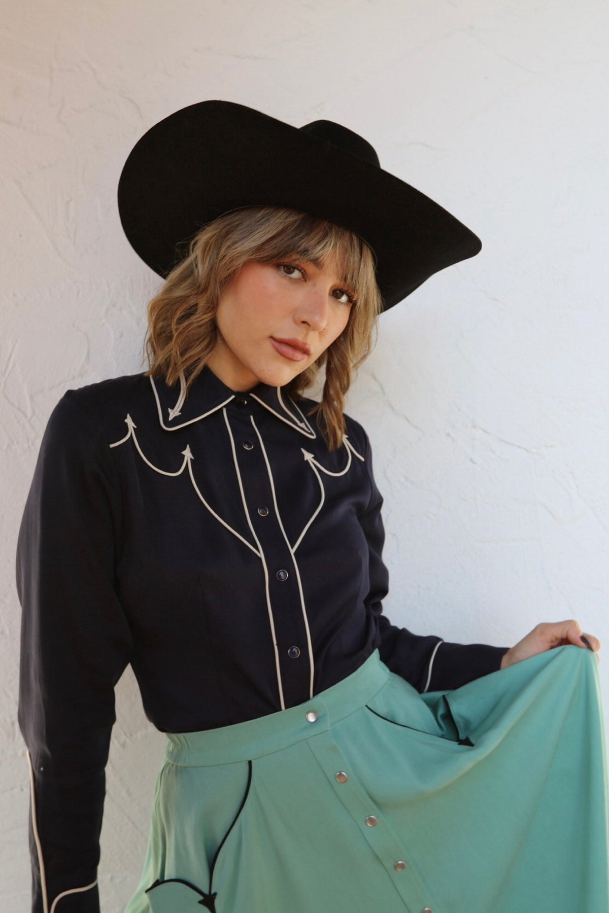 Woman in a black cowboy hat wearing the H Bar C Lake Tahoe navy western shirt with white piped yokes and a green skirt.