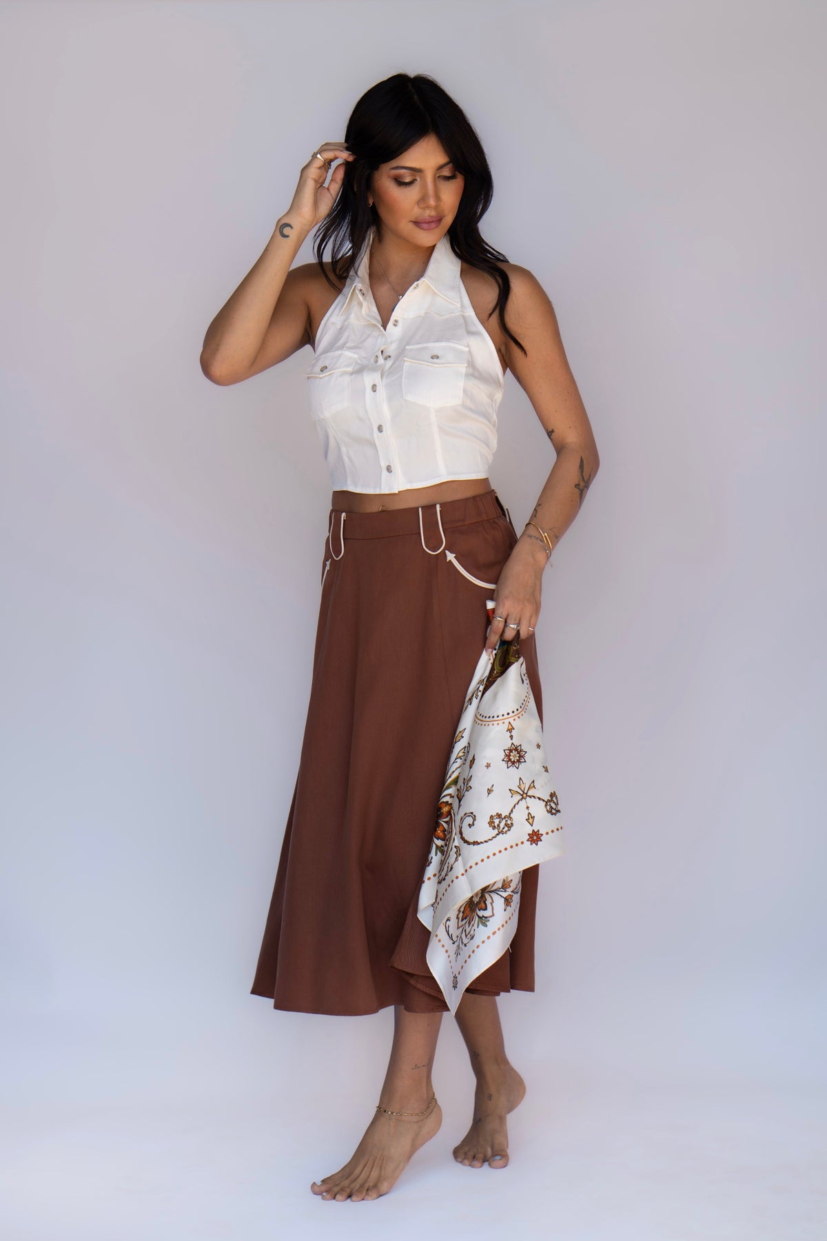 Model styling the H Bar C Ivory Calabasas silk scarf in hand with a white halter western top and brown skirt, vintage inspired western accessories.