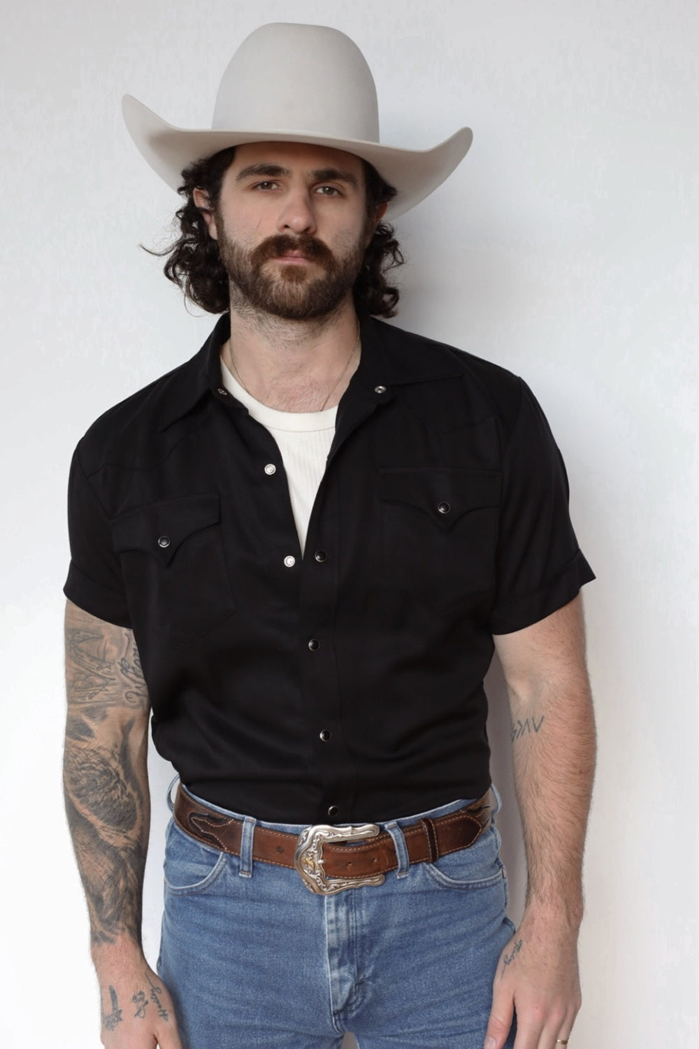 Man in a cream cowboy hat wearing the H Bar C Newport short sleeve western shirt in black with pearl snaps, tucked into jeans.