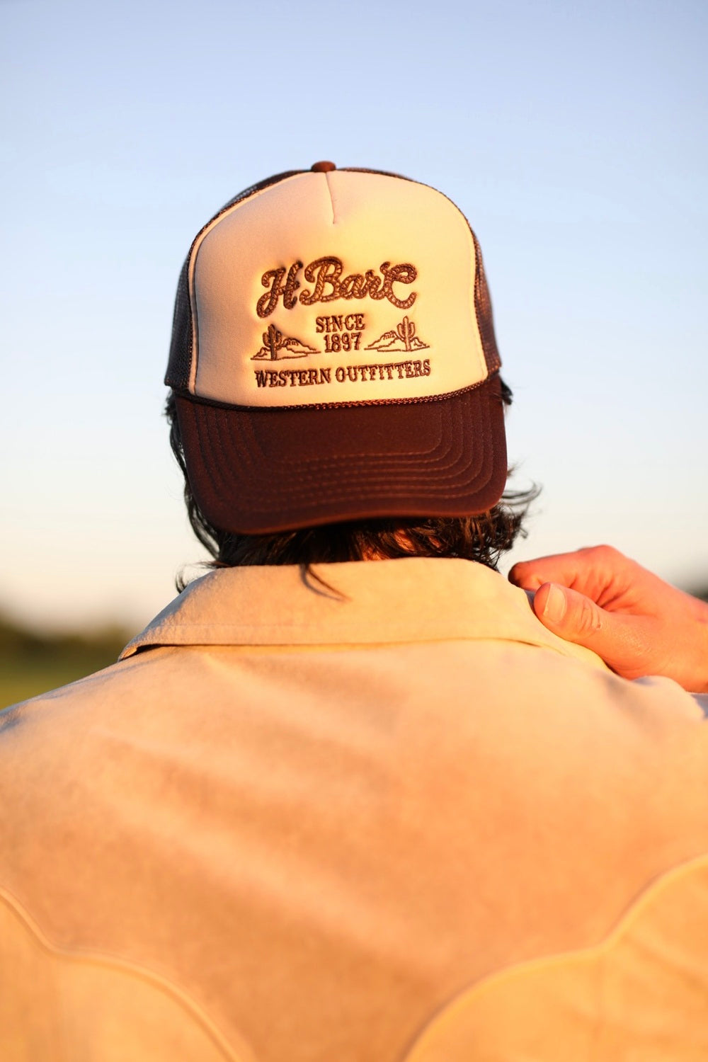 H Bar C tan rope baseball hat with Western Outfitters script worn with a western jacket.