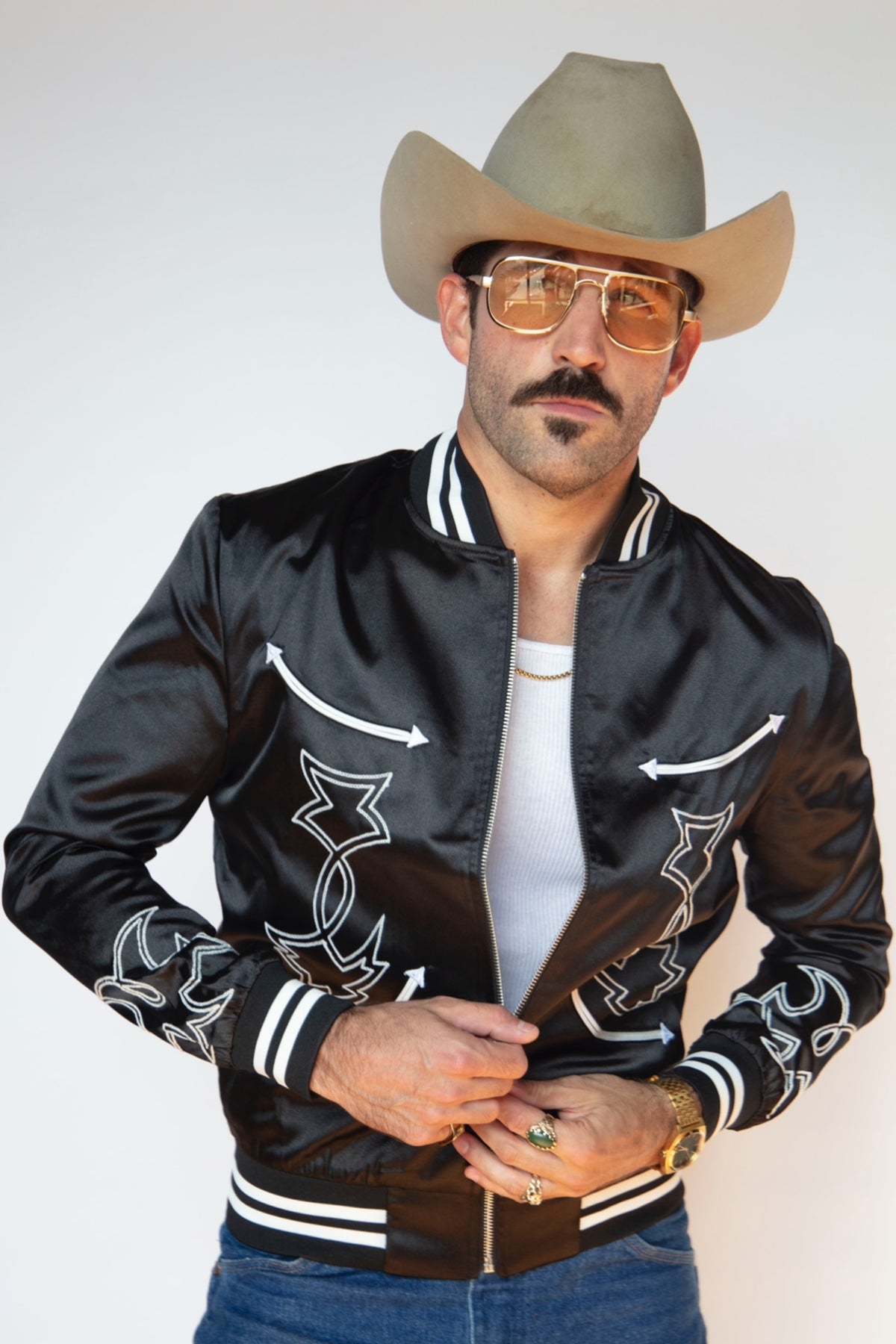Man in a cowboy hat wearing the H Bar C Odessa tour jacket in black satin with white embroidery and striped ribbing.