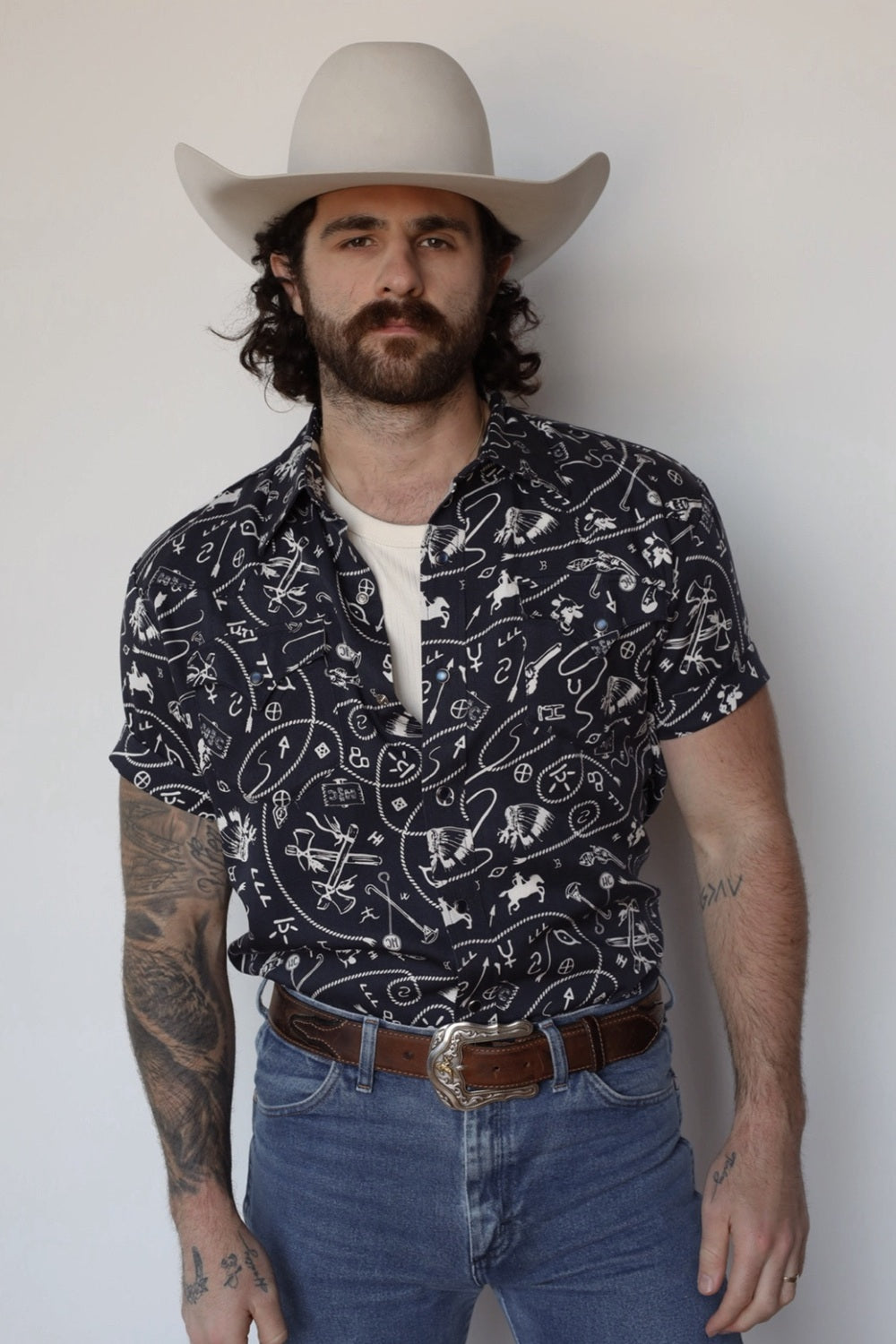 Man in a cream cowboy hat wearing the H Bar C Newport Rockridge short sleeve shirt in navy with a white western novelty print.