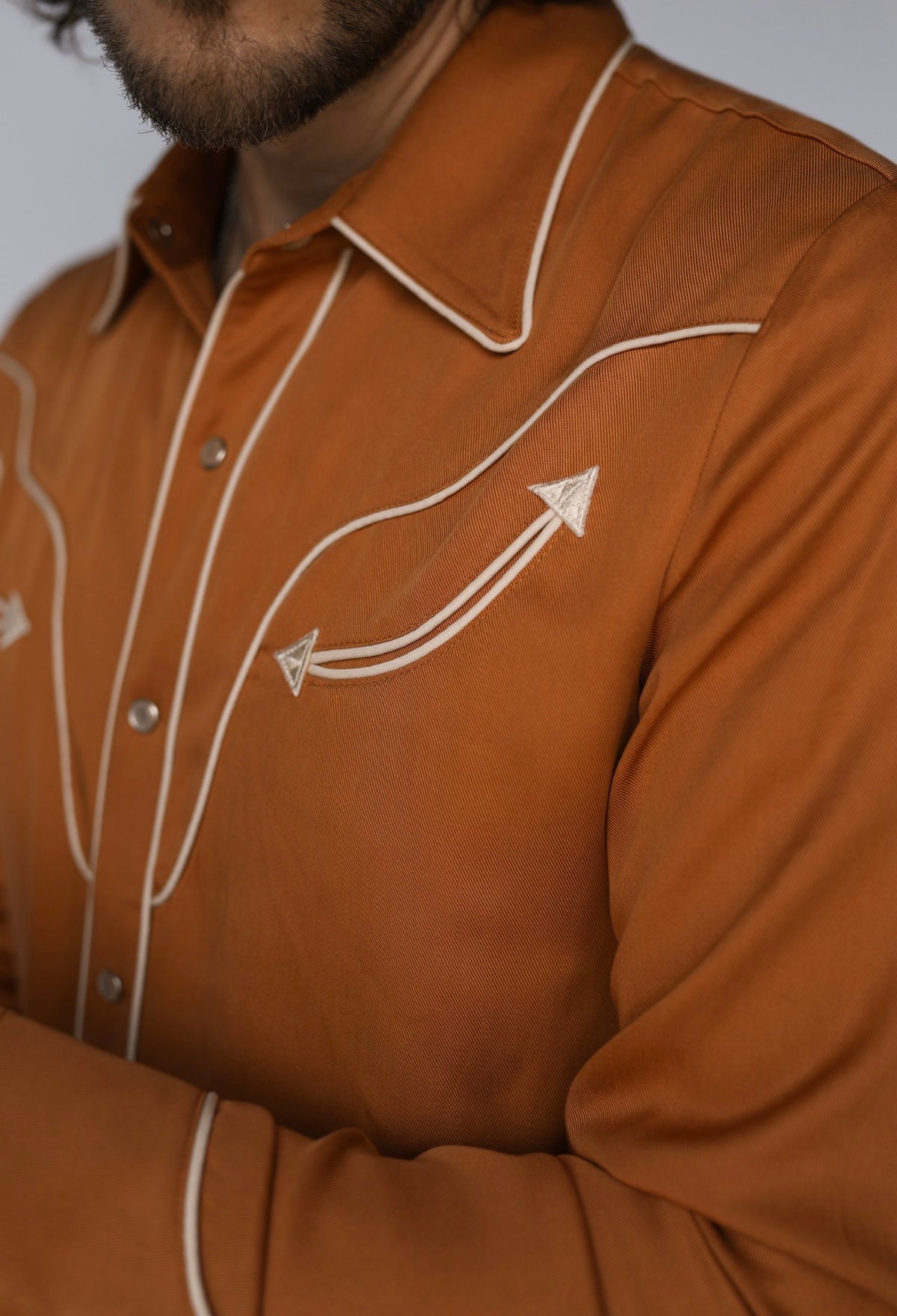 Chest detail of the H Bar C San Fernando burnt orange shirt showing cream arrow piping and snap placket.