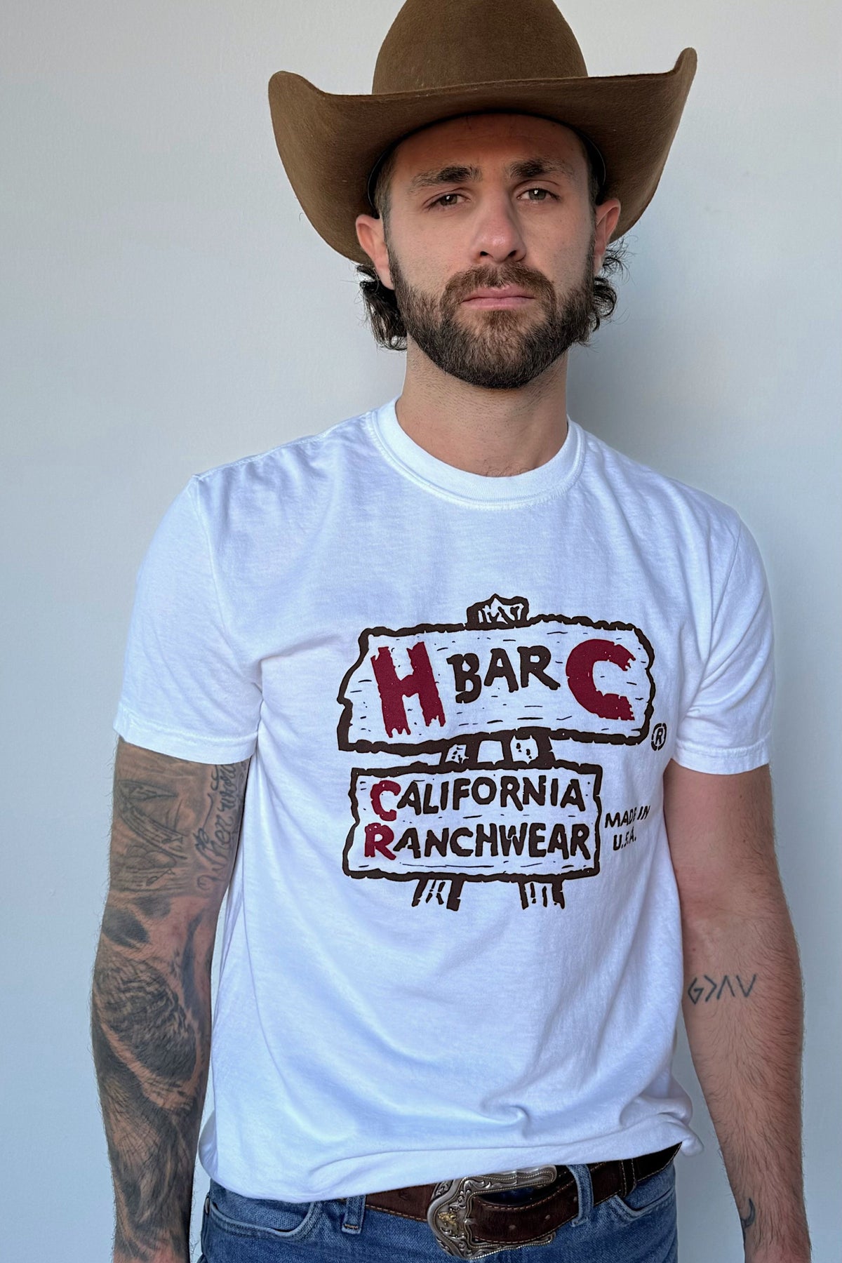 Man in a cowboy hat wearing the H Bar C Rattlesnake Junction white tee with the original H Bar C California Ranchwear logo.