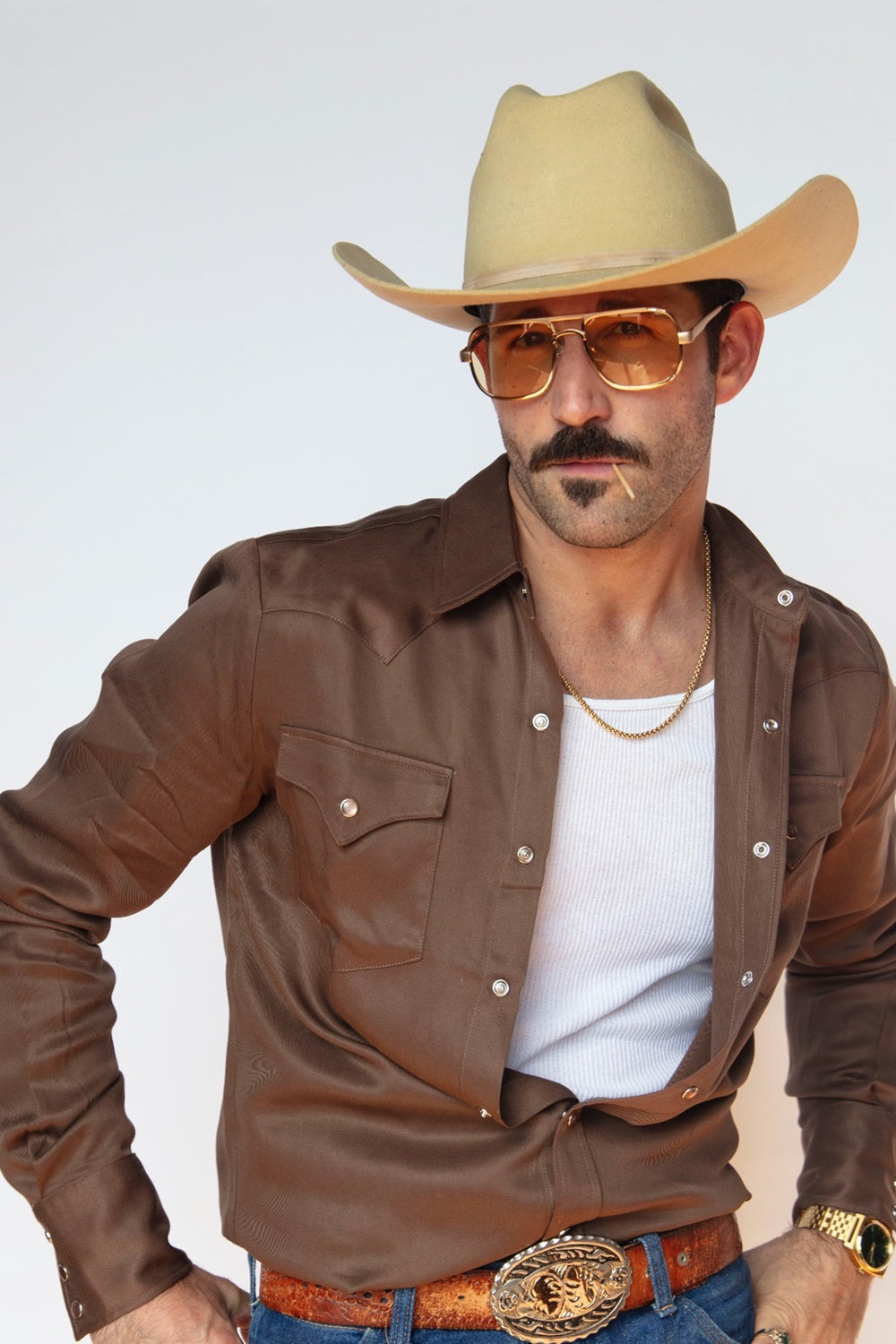 Man in a straw cowboy hat wearing the H Bar C Denver chocolate shirt open over a white tank with a gold western buckle.