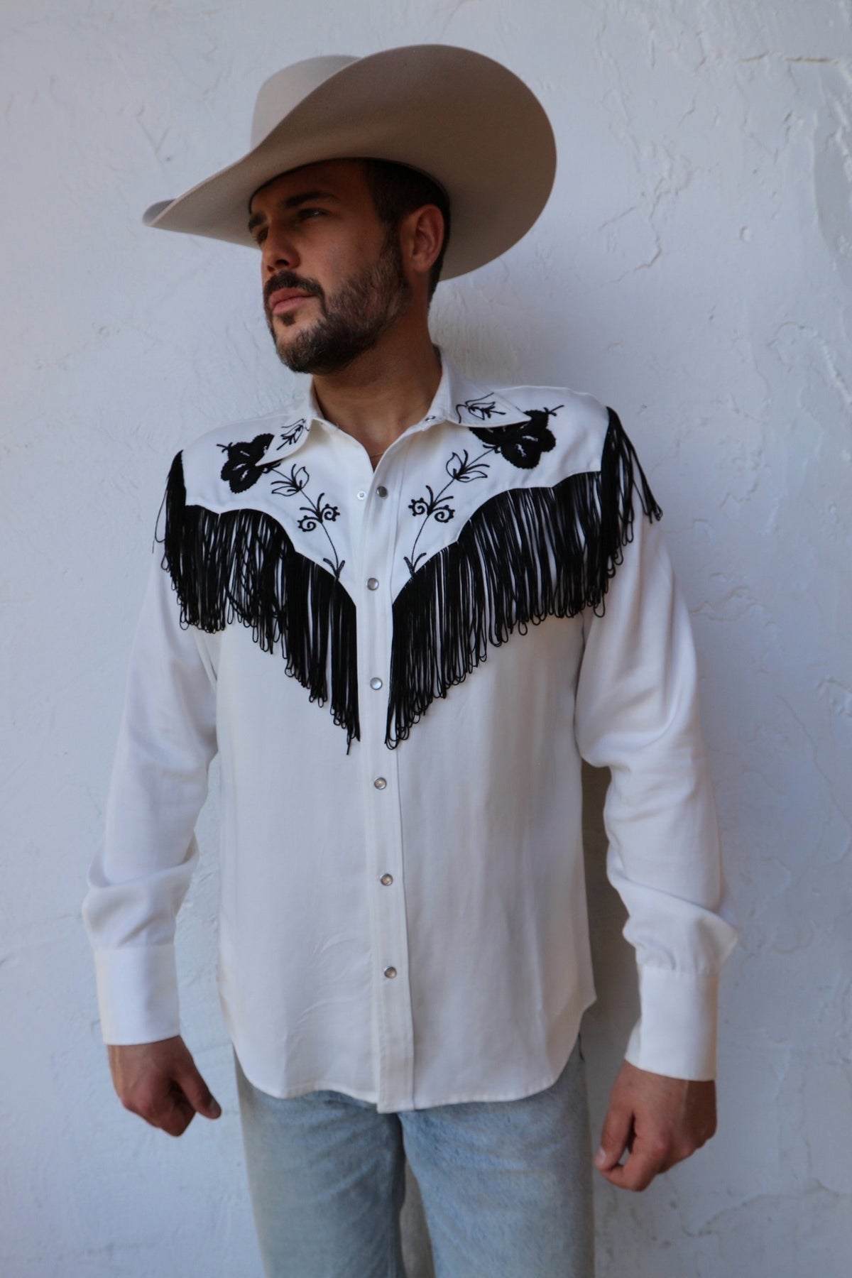 Man in a cowboy hat wearing the H Bar C Taos men's shirt in white with black fringe and black embroidered yokes.