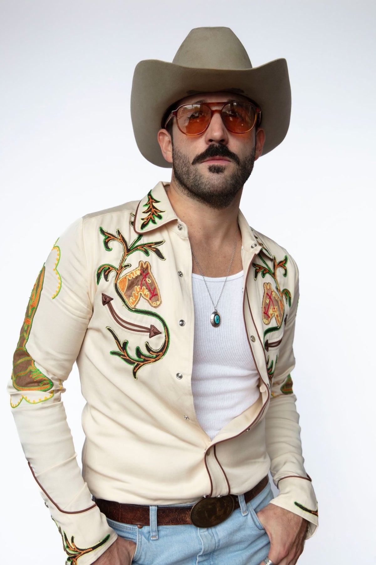 Man in a cowboy hat wearing the H Bar C Calabasas shirt in off-white, a 1940s remake with multicolor chain stitch embroidery.