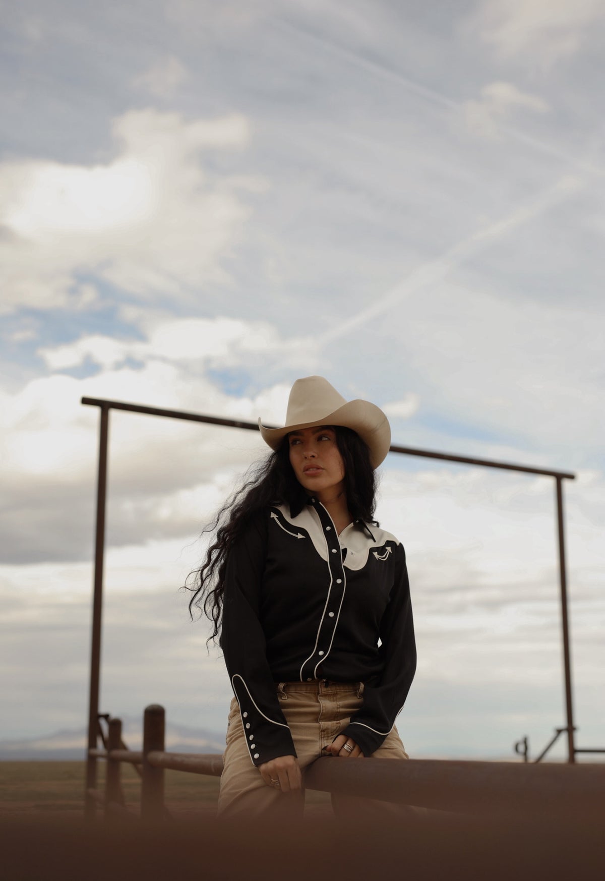 Woman standing under a ranch gate in the H Bar C San Juan women's black western shirt.