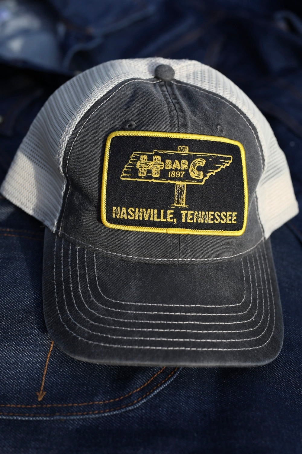 Close-up of the H Bar C Nashville, Tennessee signpost patch on the black mesh trucker hat.