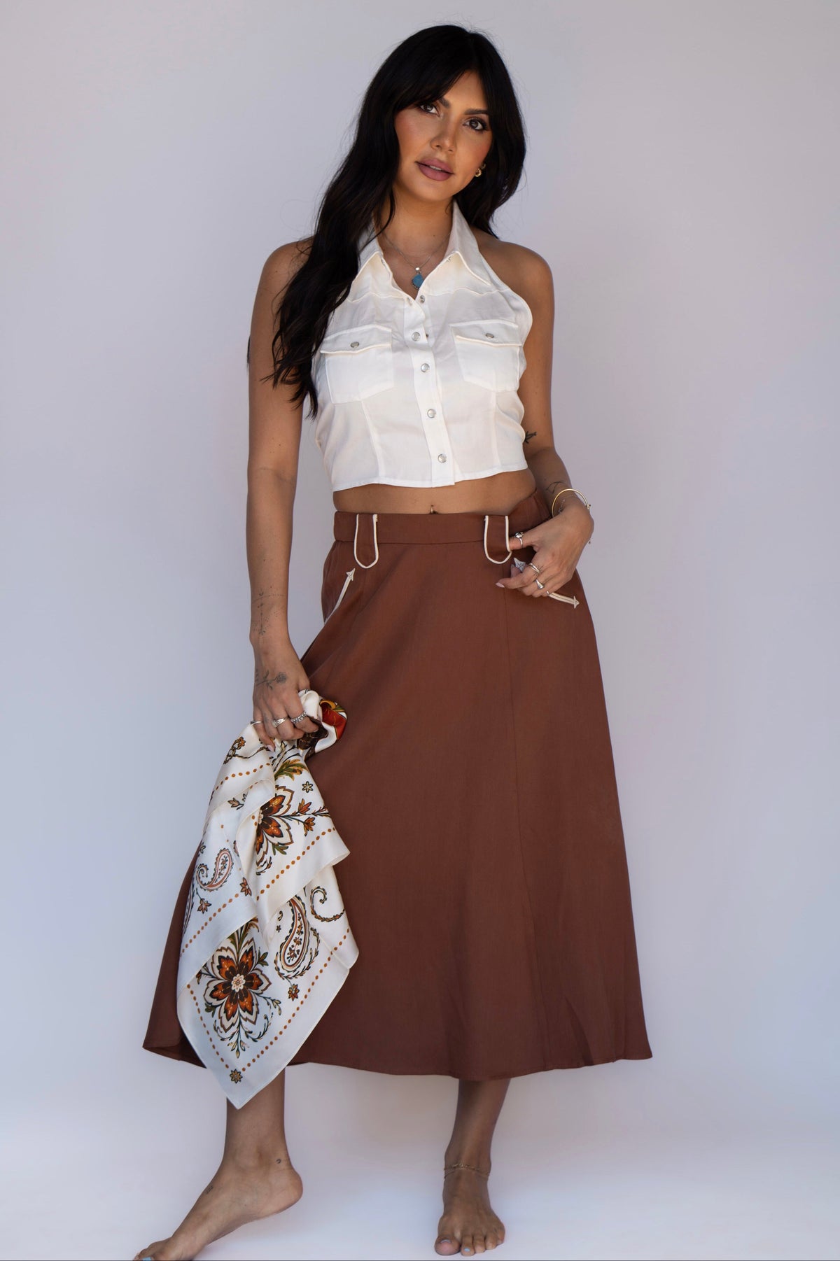 Woman wearing the H Bar C Santa Fe women's skirt in chocolate with white piped pockets, styled with the white Hampton halter and a silk scarf.