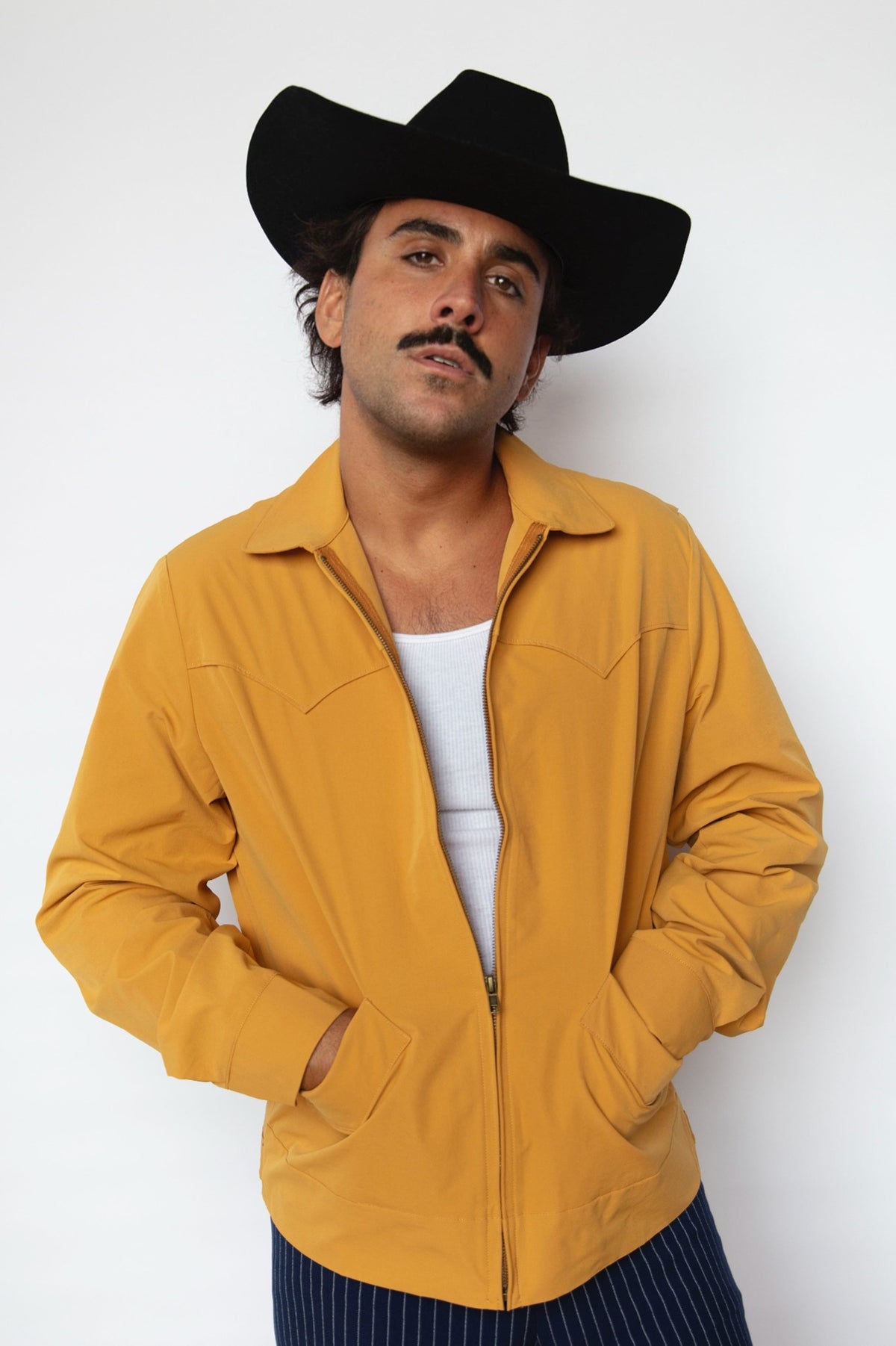 Man in a black cowboy hat wearing the H Bar C Mustang jacket in mustard yellow, a zip western jacket from the 1957 H Bar C Mustang collection.