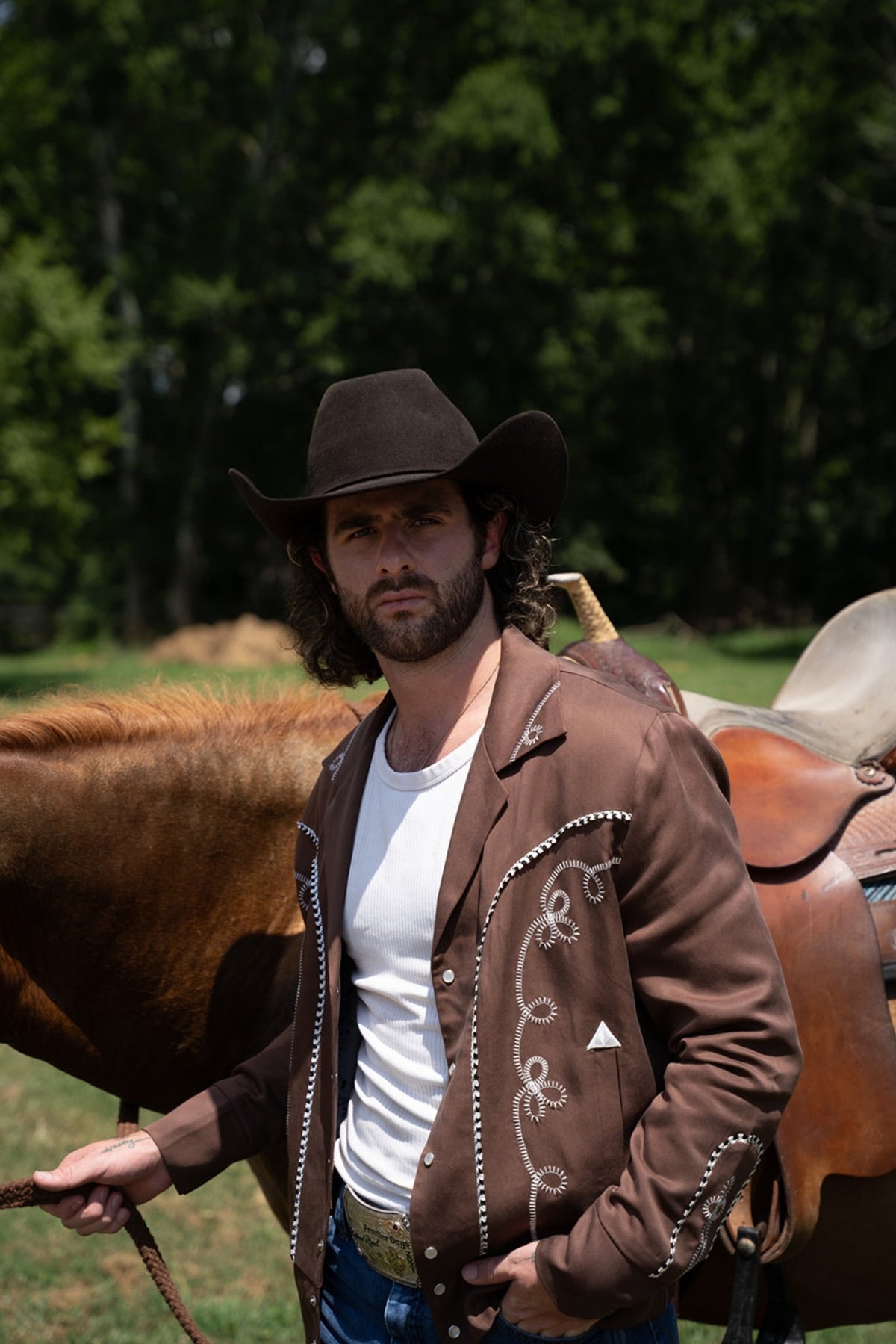 Man in a brown hat beside a horse wearing the H Bar C Bolero walnut jacket with white embroidery and a white tank.